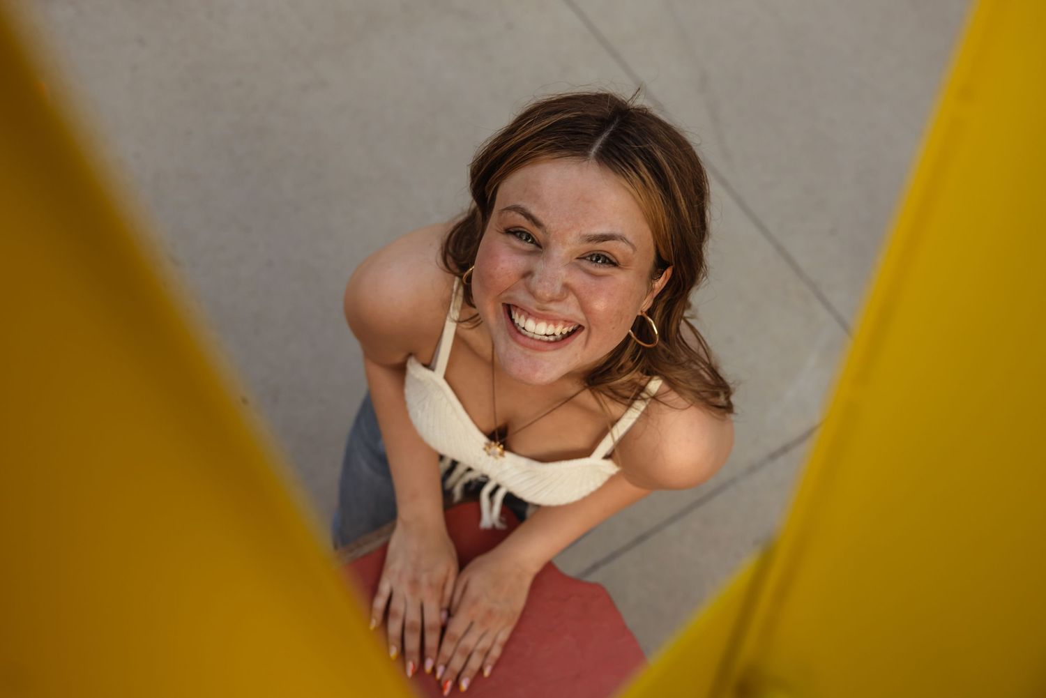 High angle view of smiling person in pink pants and white top looking up at camera against gray wall.