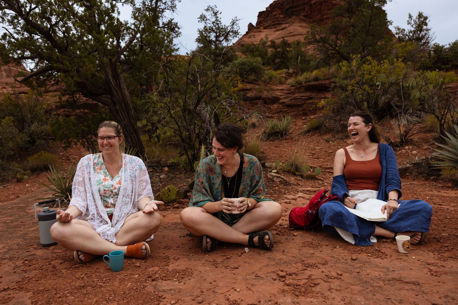 Sisters of the non-profit organization sit cross-legged on red desert ground with a sandstone formation and desert plants in the background.
