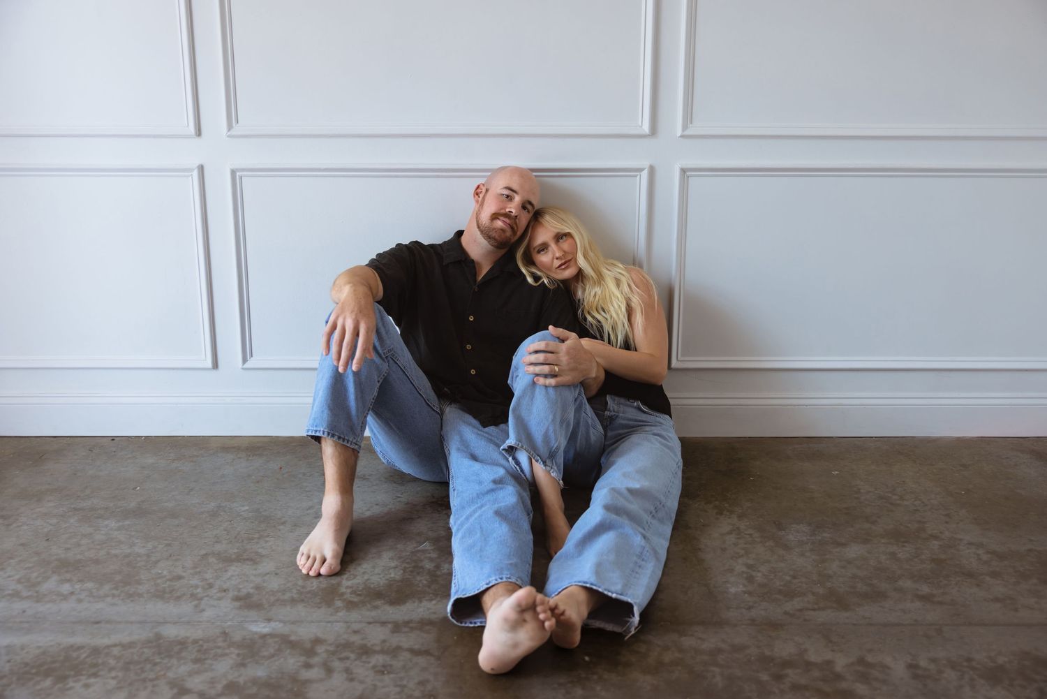 Couple denim sitting close together on floor against white paneled wall.