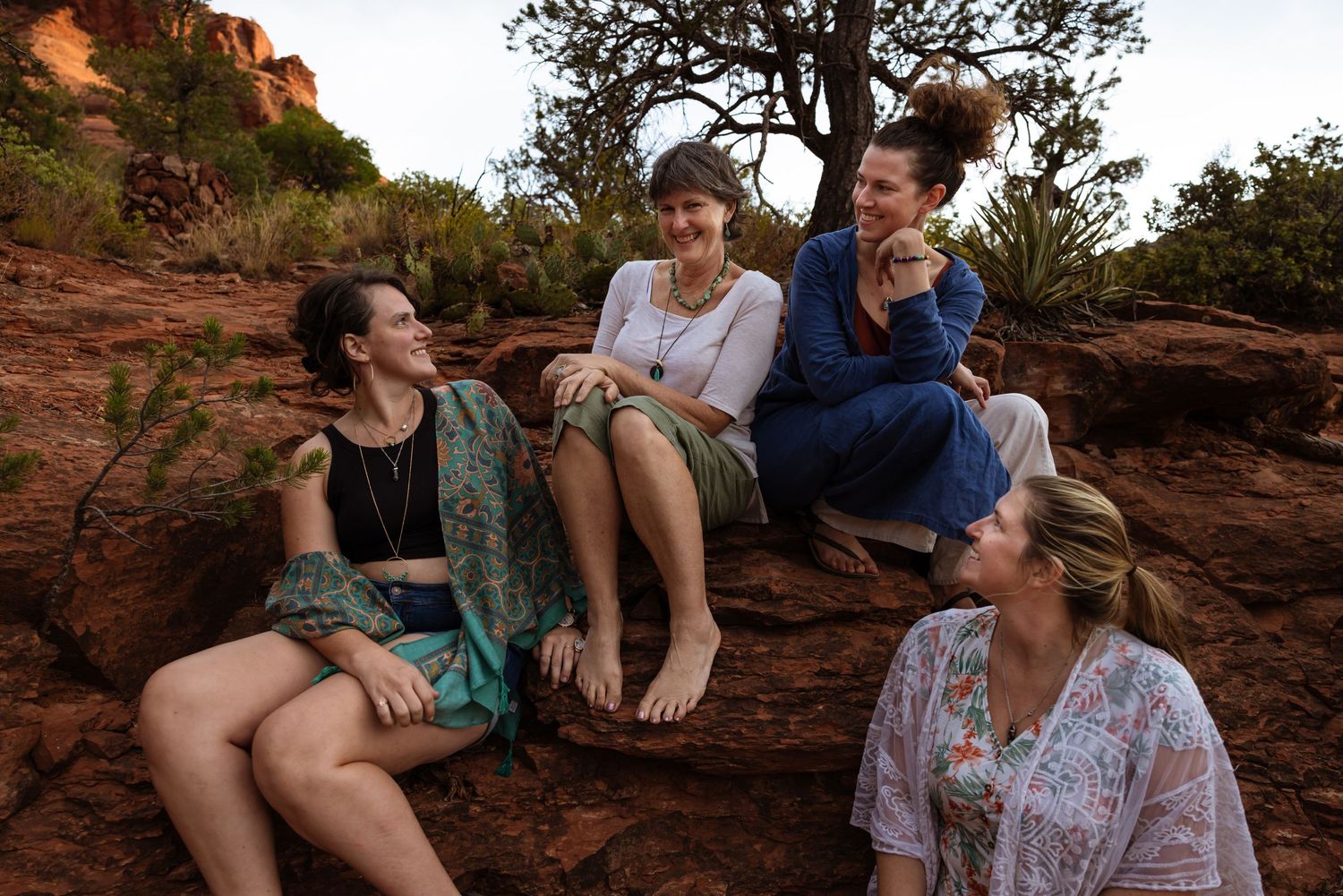 A mother and her daughters enjoy a joyful moment while sitting on red rocks during sunset in Sedona.