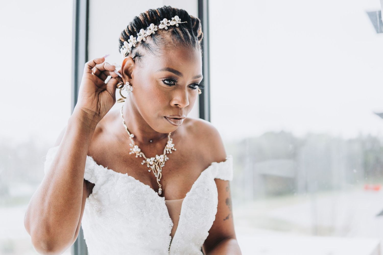 Elegant bride wearing a strapless white wedding gown with delicate crystal necklace and hairpiece in sunlit room.