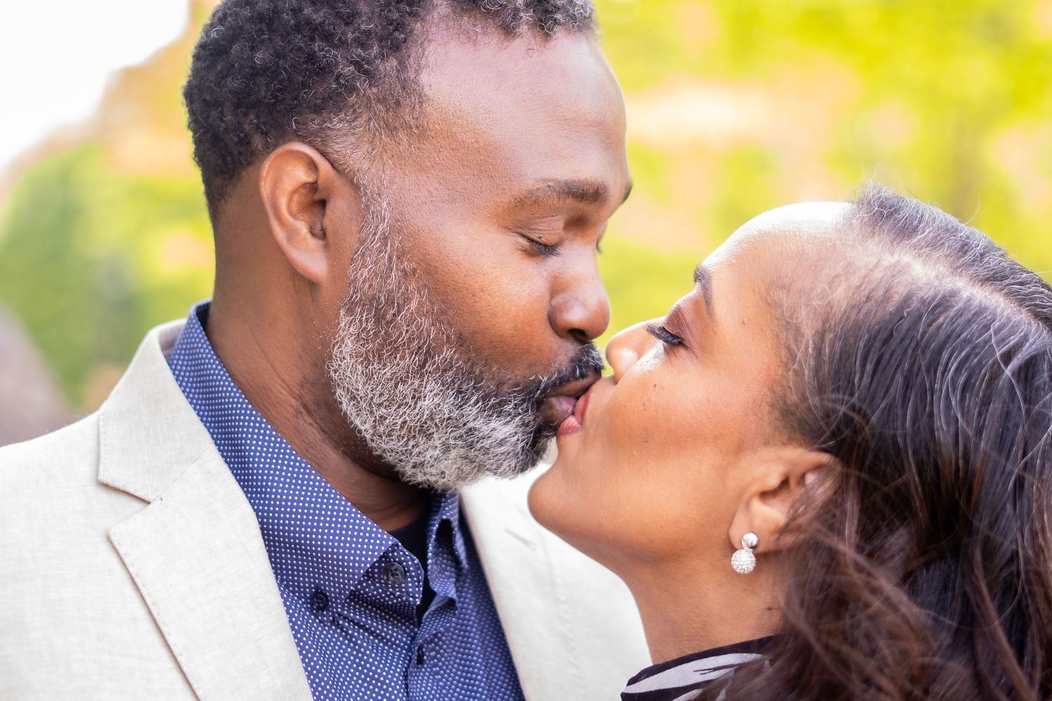 A romantic couple kisses tenderly in an outdoor setting with natural lighting.