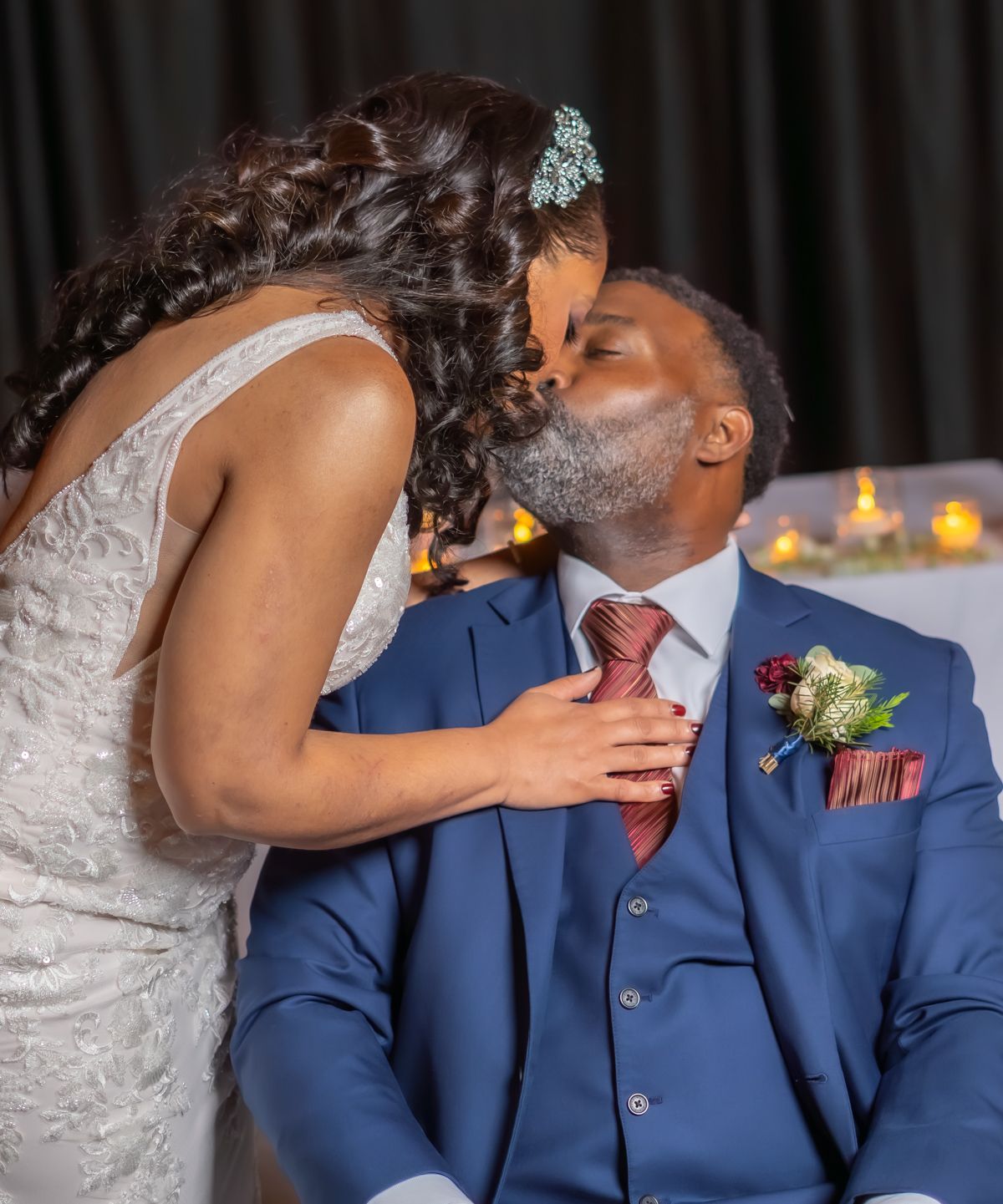 A romantic moment between newlyweds sharing a kiss, with the groom in a blue suit and bride in a white lace dress.