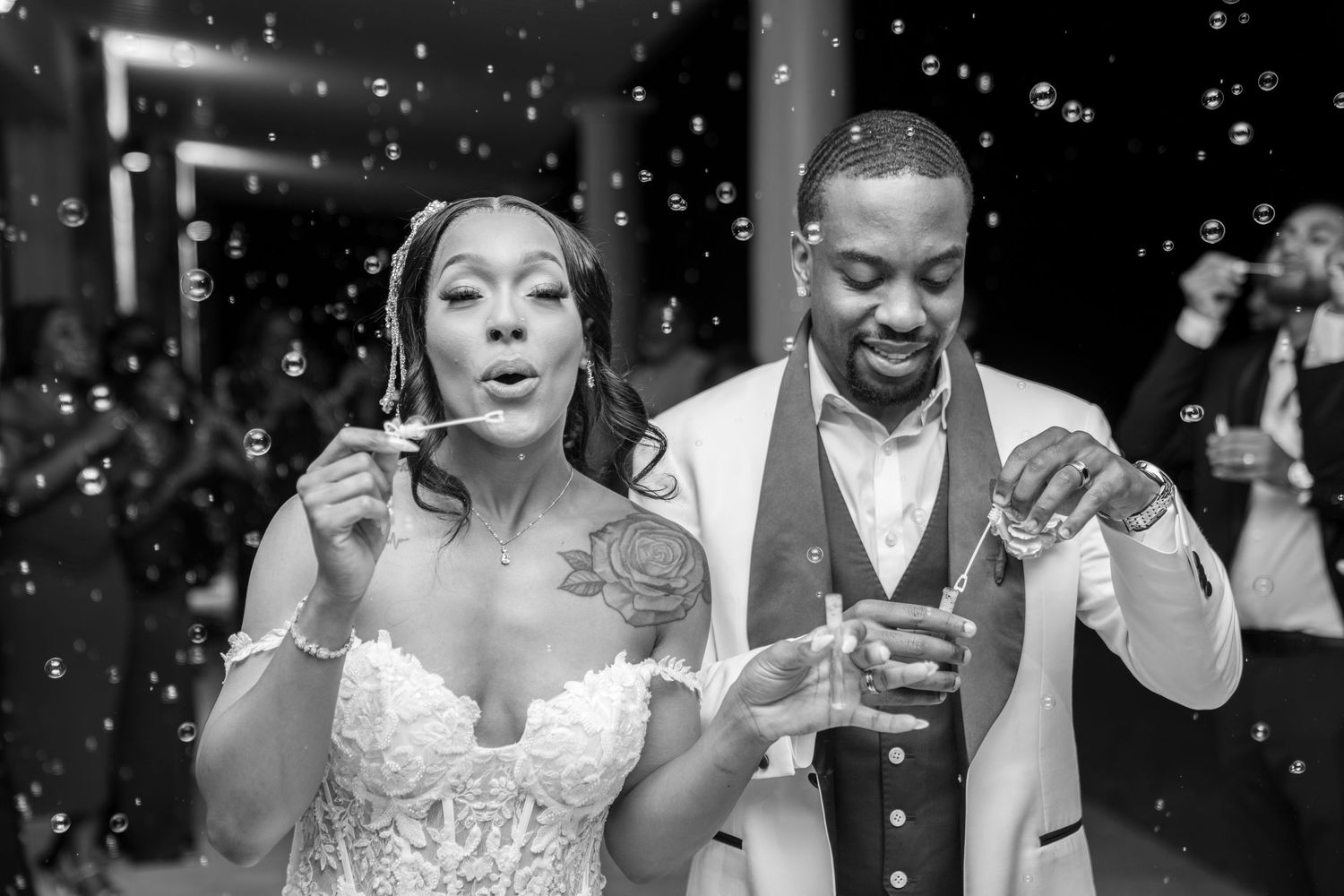Black and white photo of a bride and groom blowing bubbles together at their wedding reception.