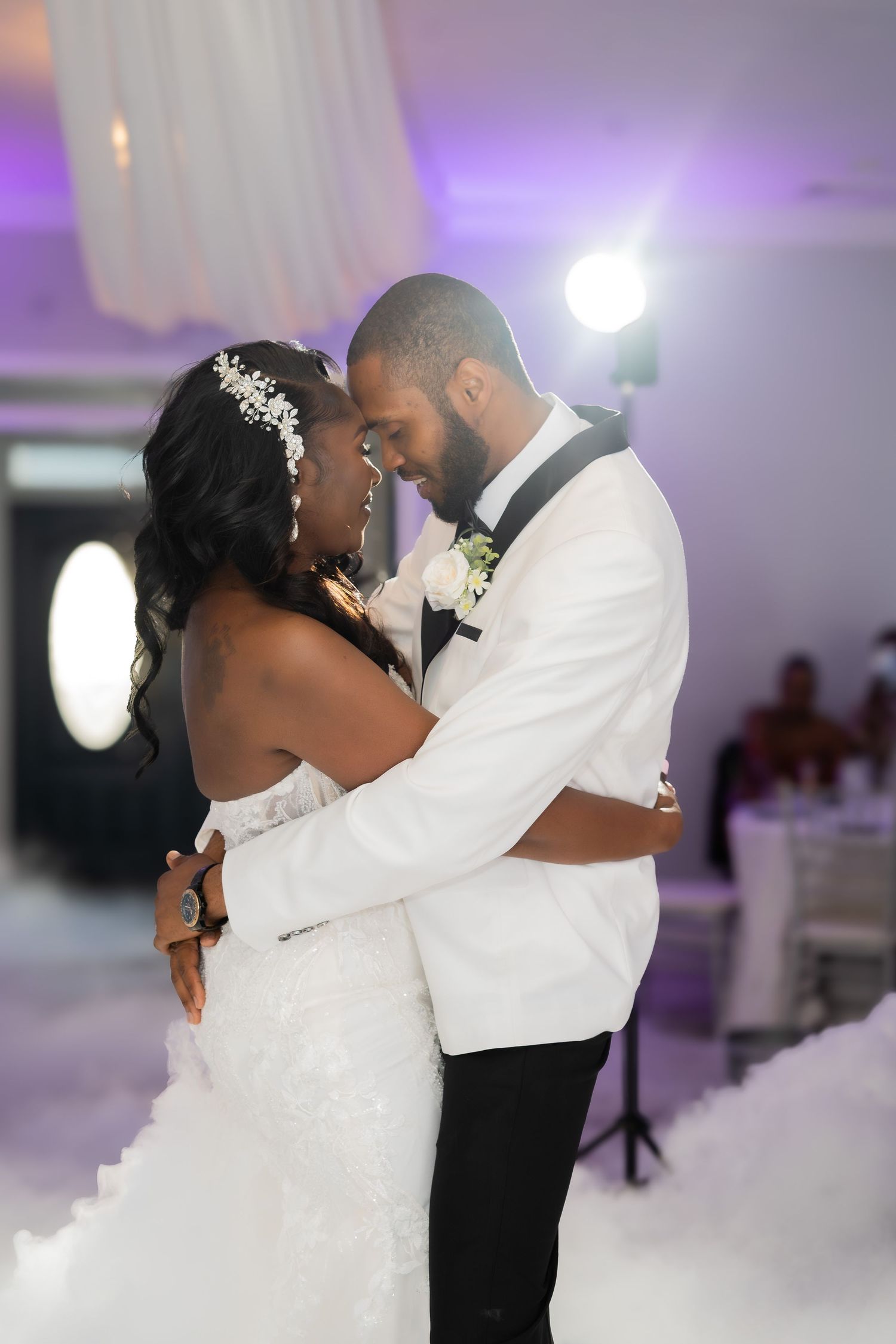 Tender moment between newlyweds during first dance with purple lighting and fog effects.