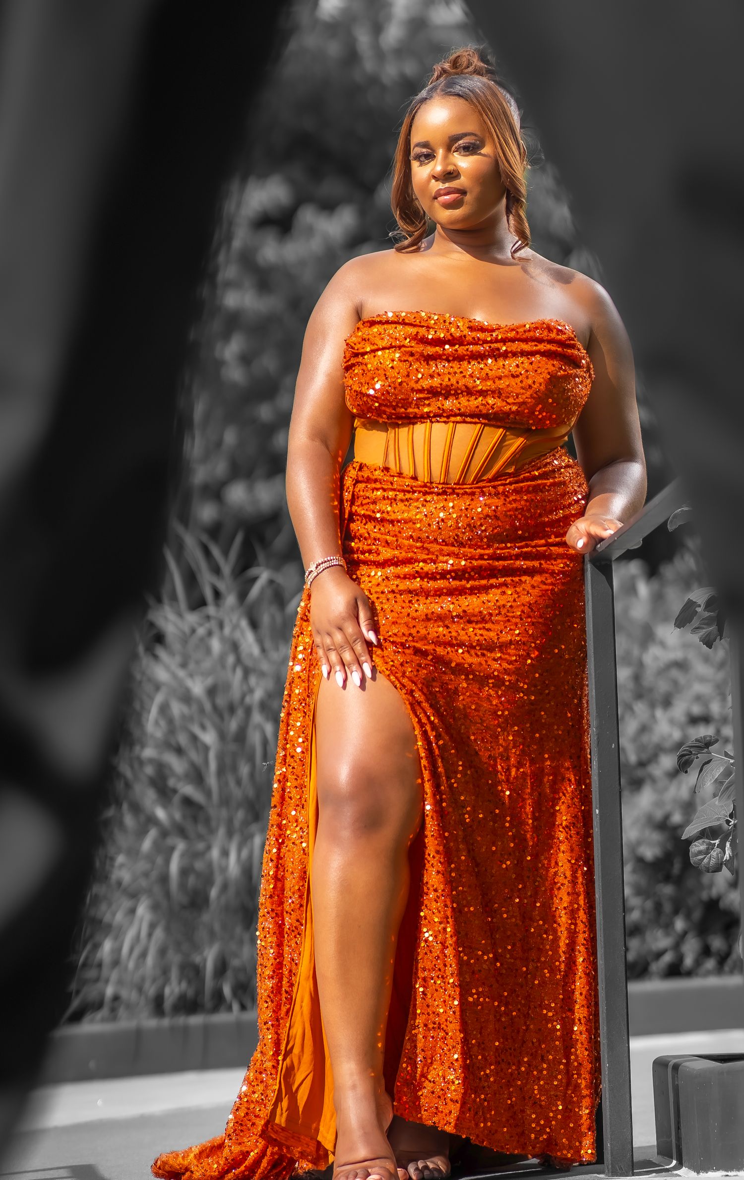 Woman in orange sequin strapless crop top and maxi skirt with slit poses confidently outdoors.