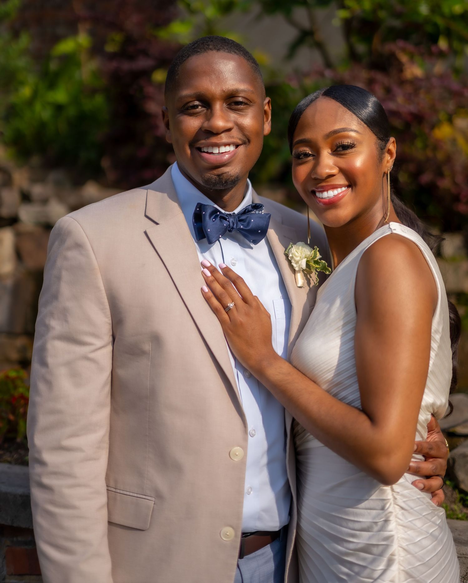 A happy couple embraces outdoors in formal attire with natural foliage in the background.