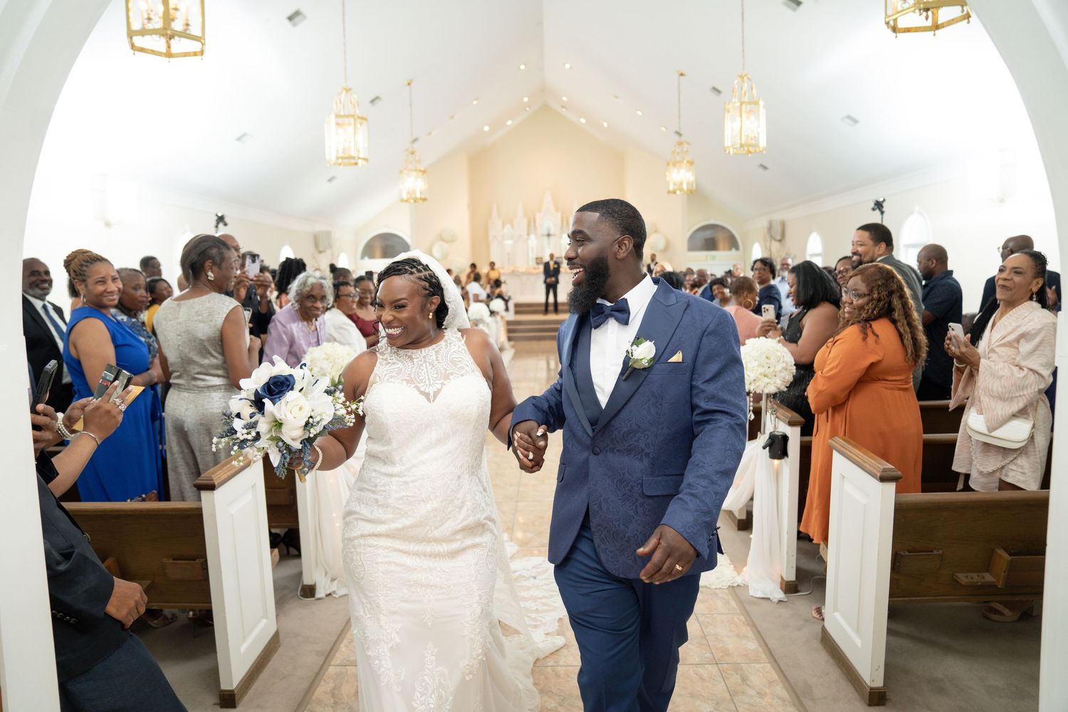 Wedding guests gather in a bright church sanctuary with white columns and warm lighting during a ceremony.