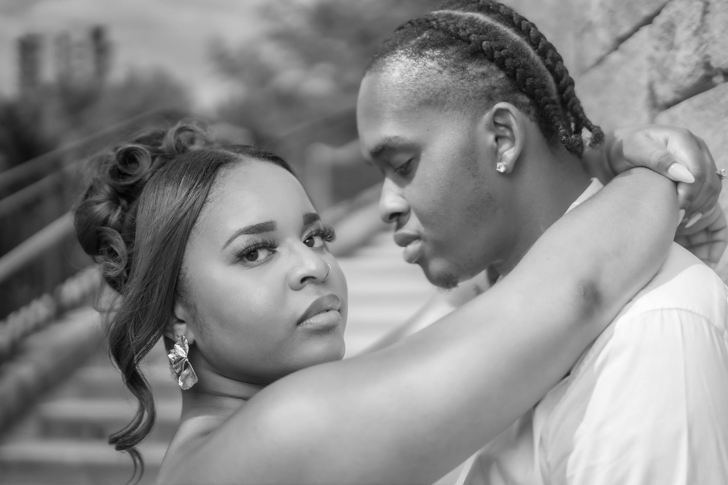 Black and white portrait of a couple embracing tenderly, woman with elegant updo and chandelier earrings, man with braided hair.