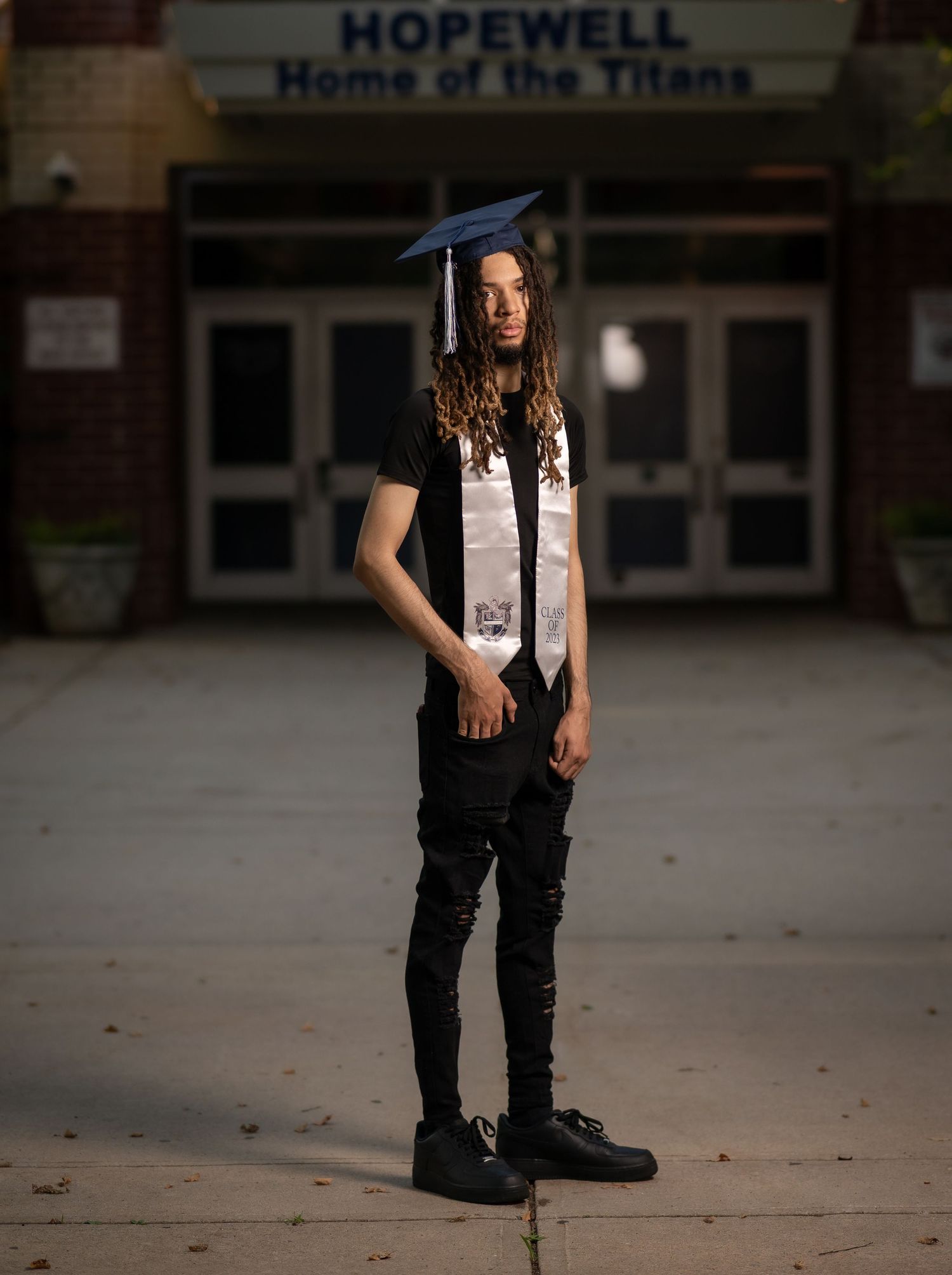 Graduate in cap and gown poses outside Hopewell High School for senior portraits at dusk.