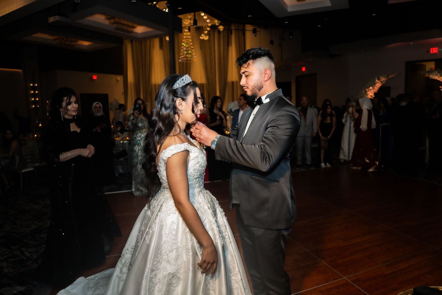 A bride and groom share their first dance together on a dimly lit ballroom floor during their wedding reception.