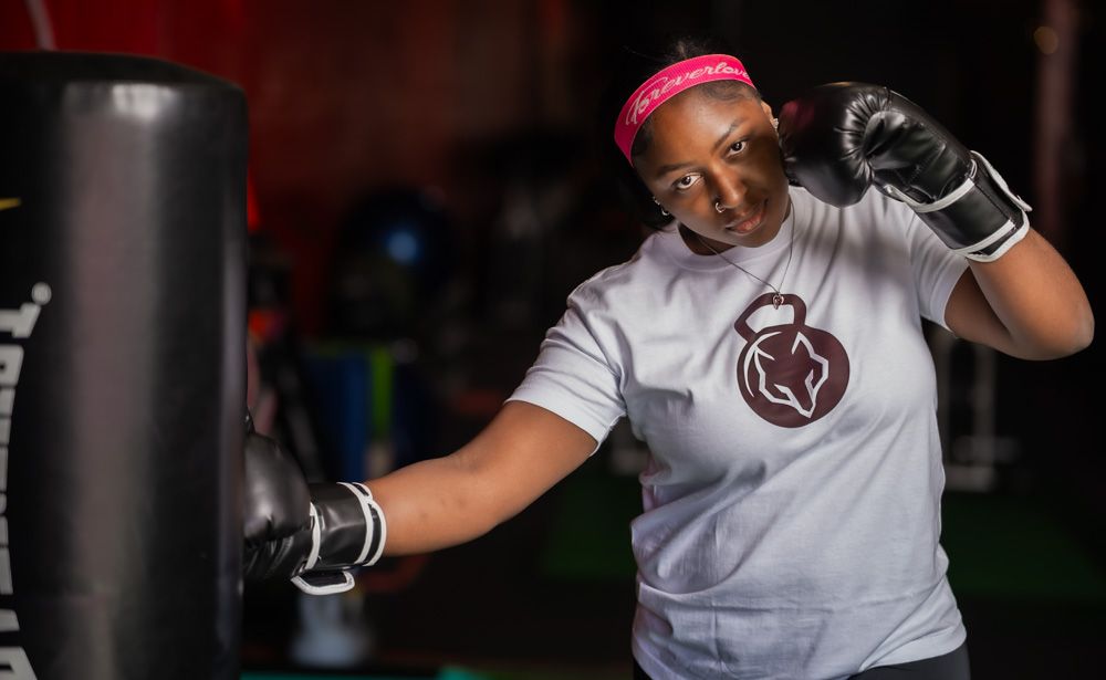A person wearing a white t-shirt and pink headband performs an exercise routine in a gym setting.