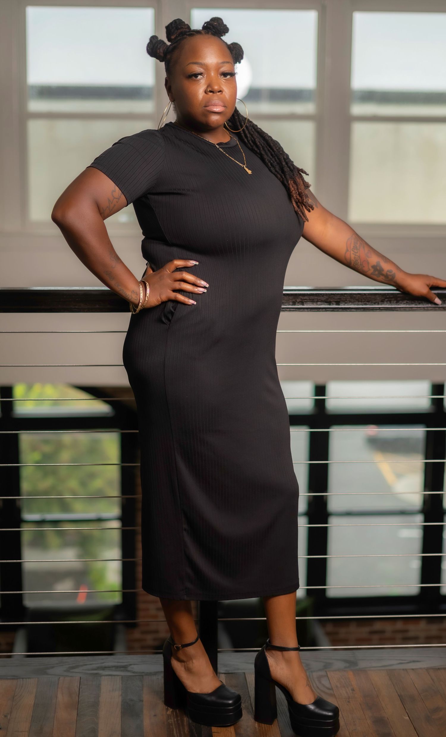 Person in a little black dress poses confidently on an outdoor balcony during a professional photoshoot.