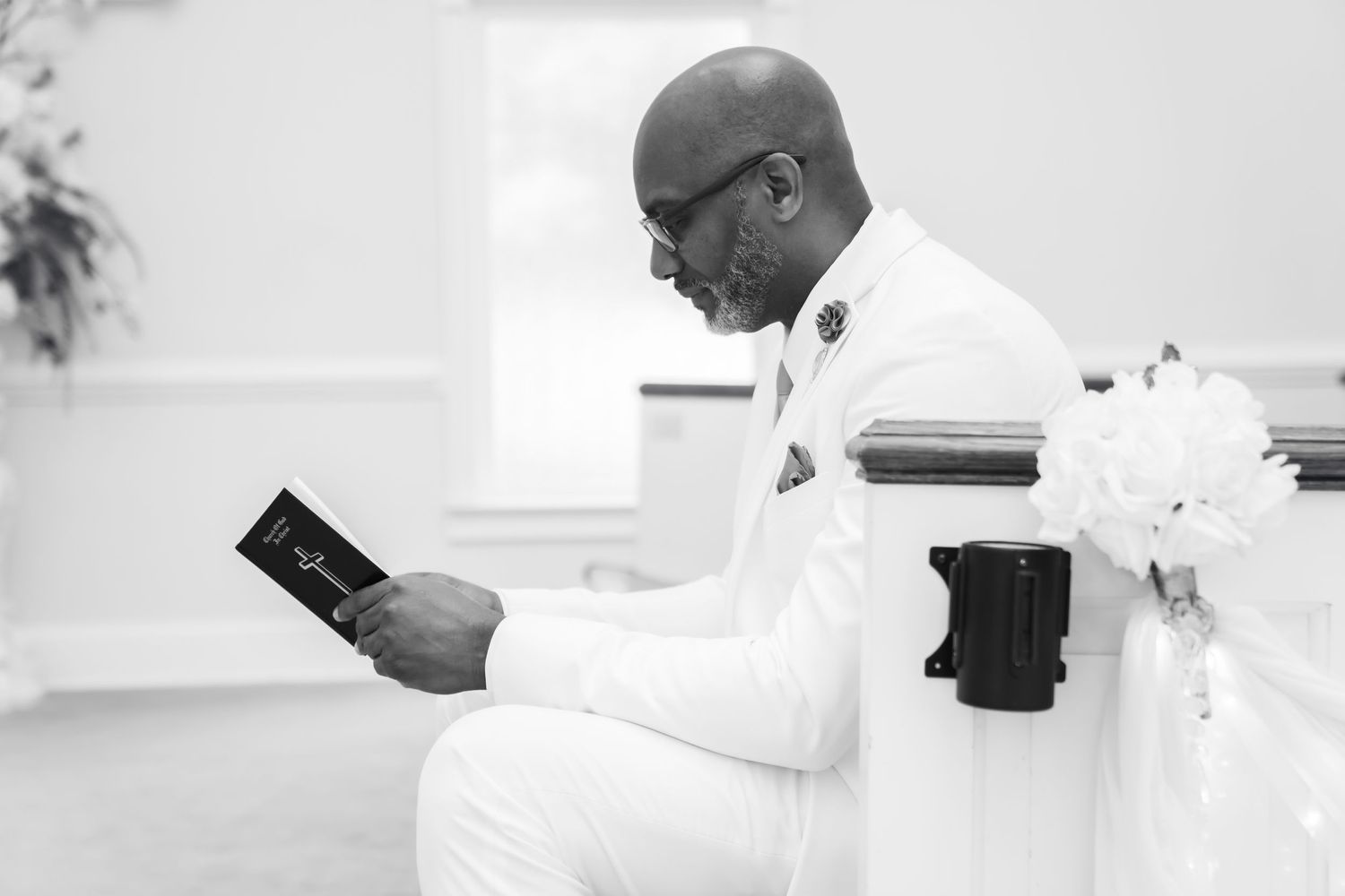 A person in a white outfit sits reading a book with a coffee cup nearby in a minimalist black and white setting.