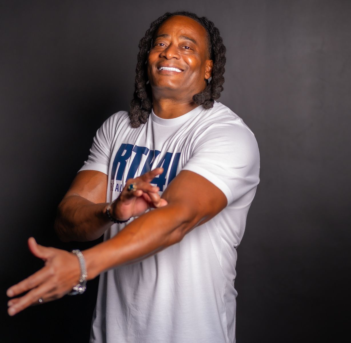 Person in white t-shirt posing against dark background with expressive gestures and bright smile.