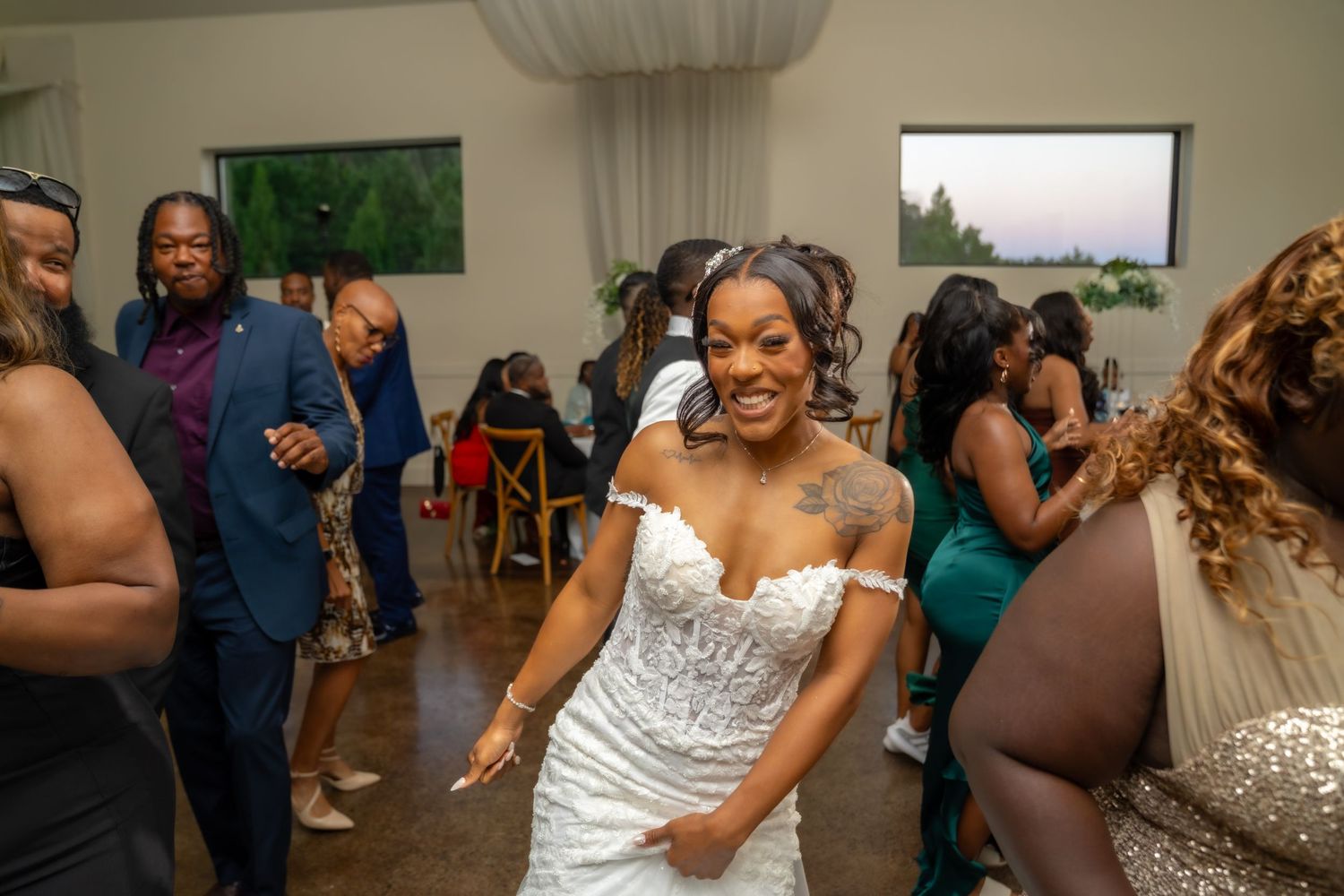Guests dancing and celebrating at a wedding reception with a person in a white strapless wedding gown in the center.