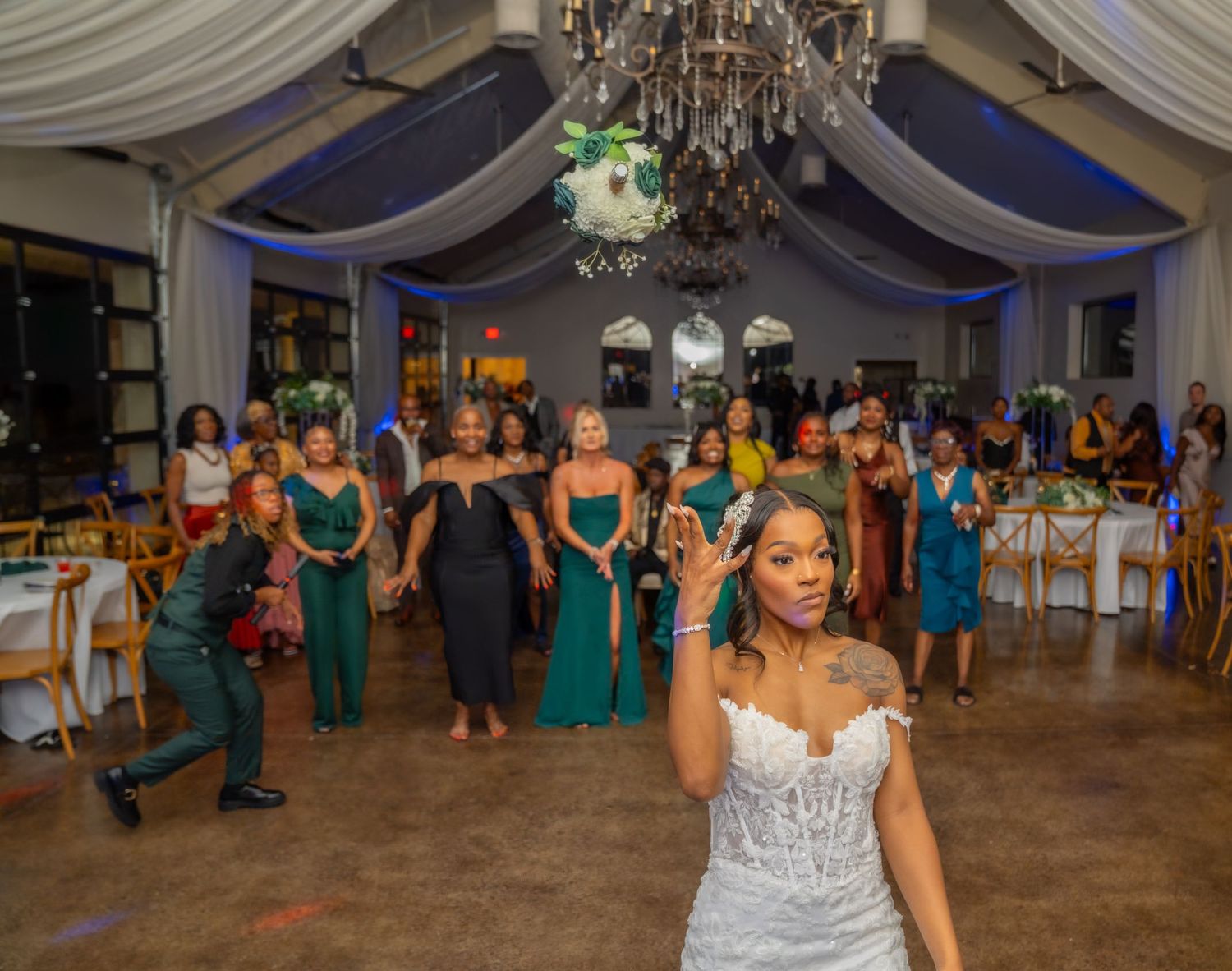 Wedding guests dance together on a reception dance floor under elegant draped fabric and chandeliers.