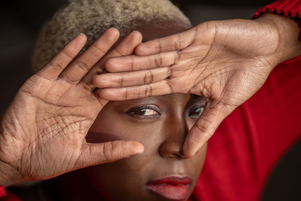 A woman in red frames her face with her hands, showcasing expressive eyes and short gray hair.