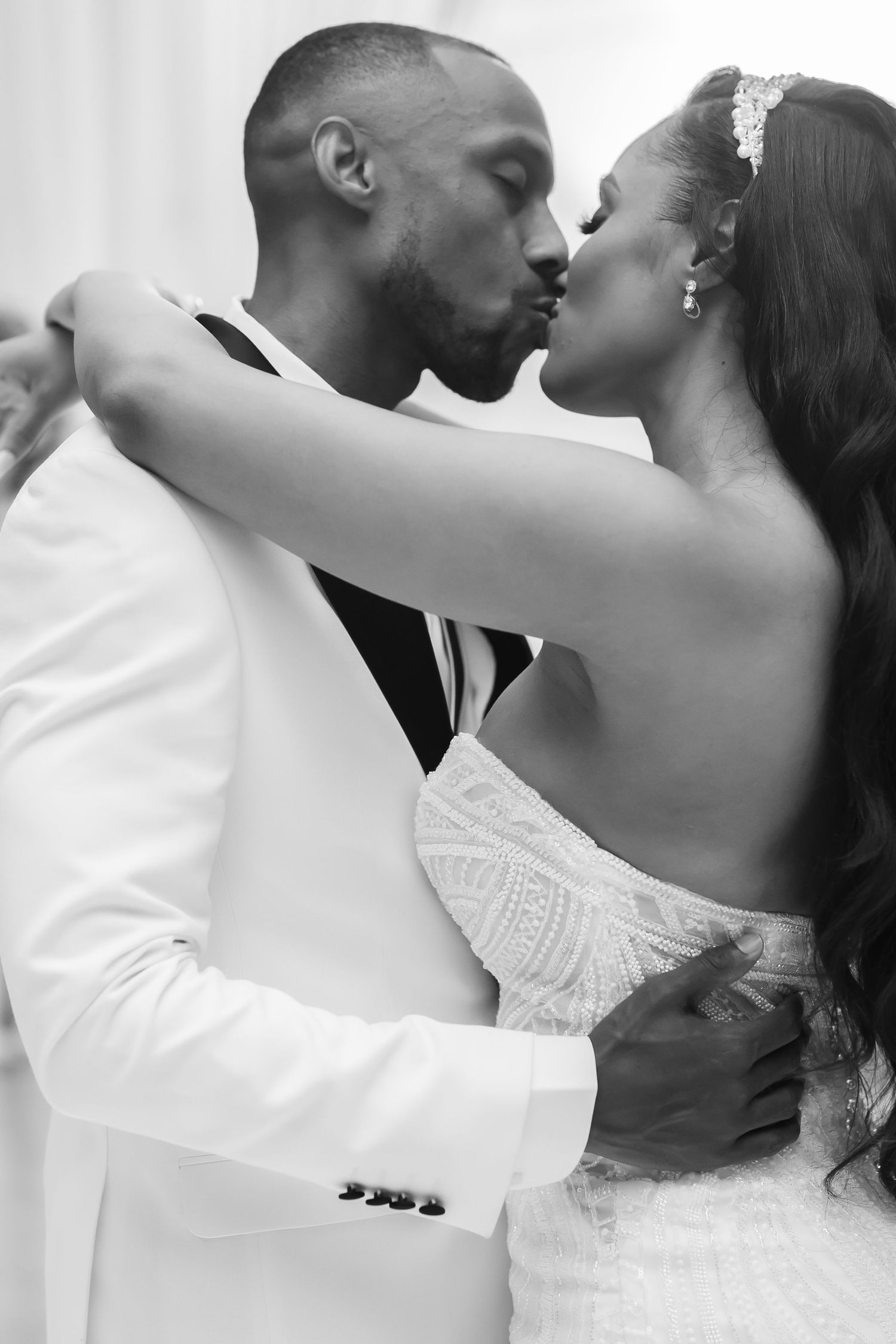 Romantic black and white wedding photo of a couple sharing an intimate kiss, with the bride in white lace and groom in white suit.