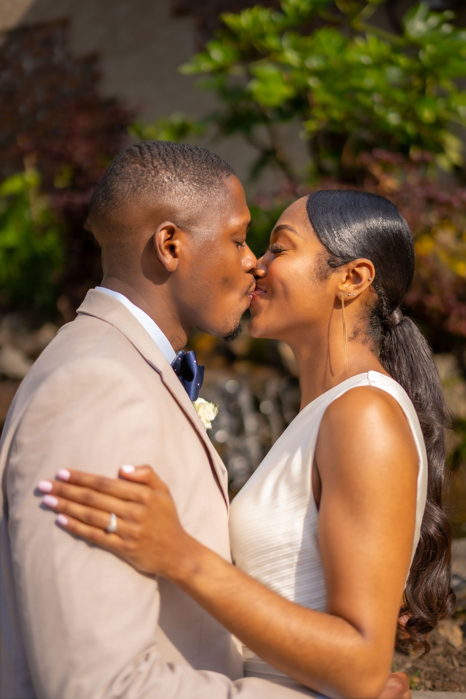 A romantic wedding couple shares a tender kiss outdoors in formal attire.