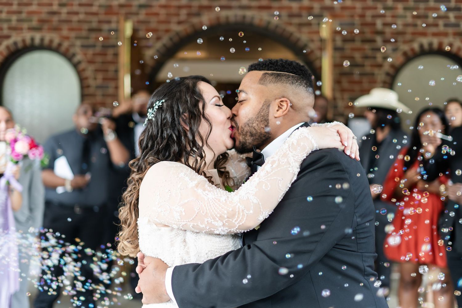 A couple shares a romantic kiss while guests shower them with white confetti at a wedding celebration.