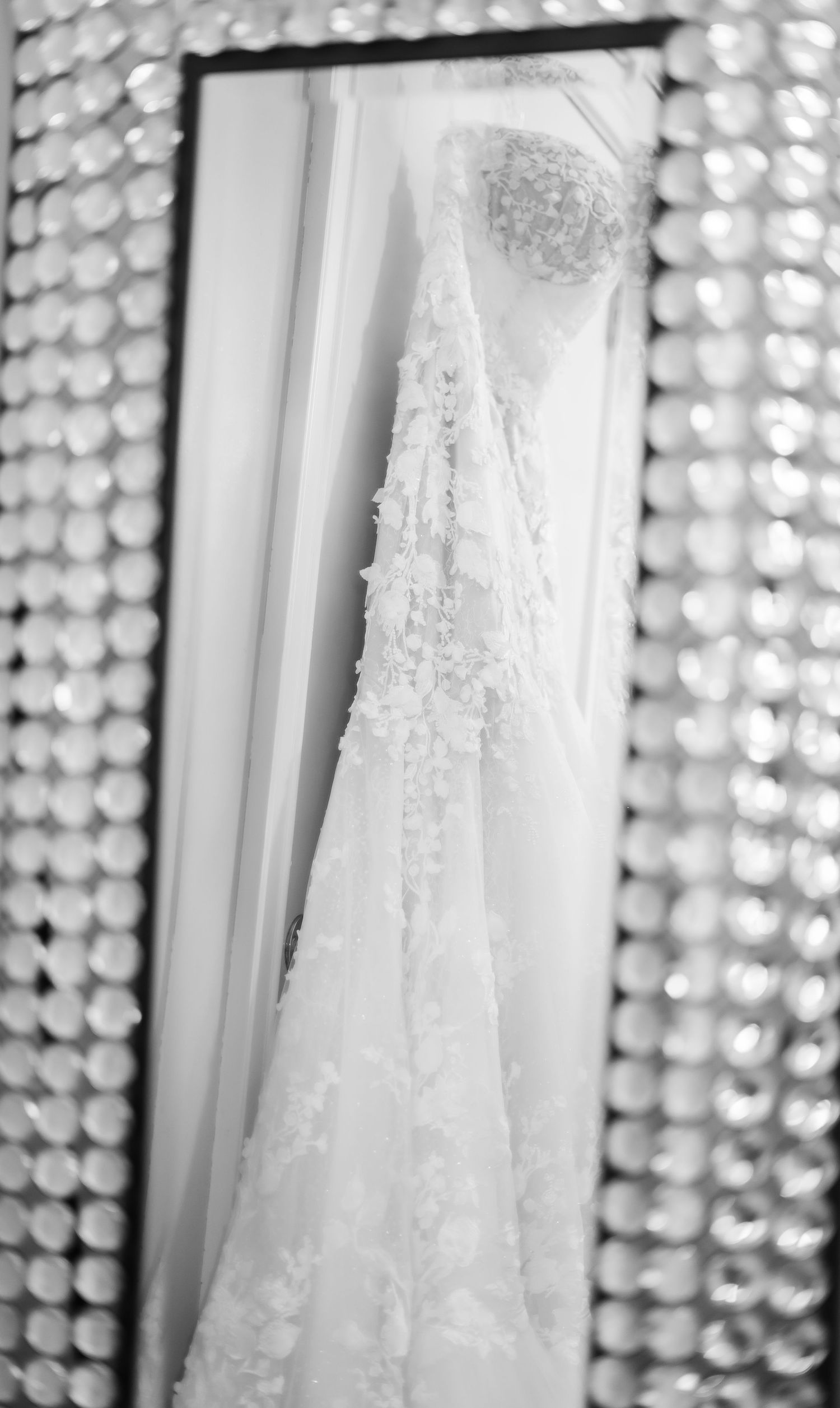 Elegant white lace wedding dress hanging against bokeh light background in black and white photography.