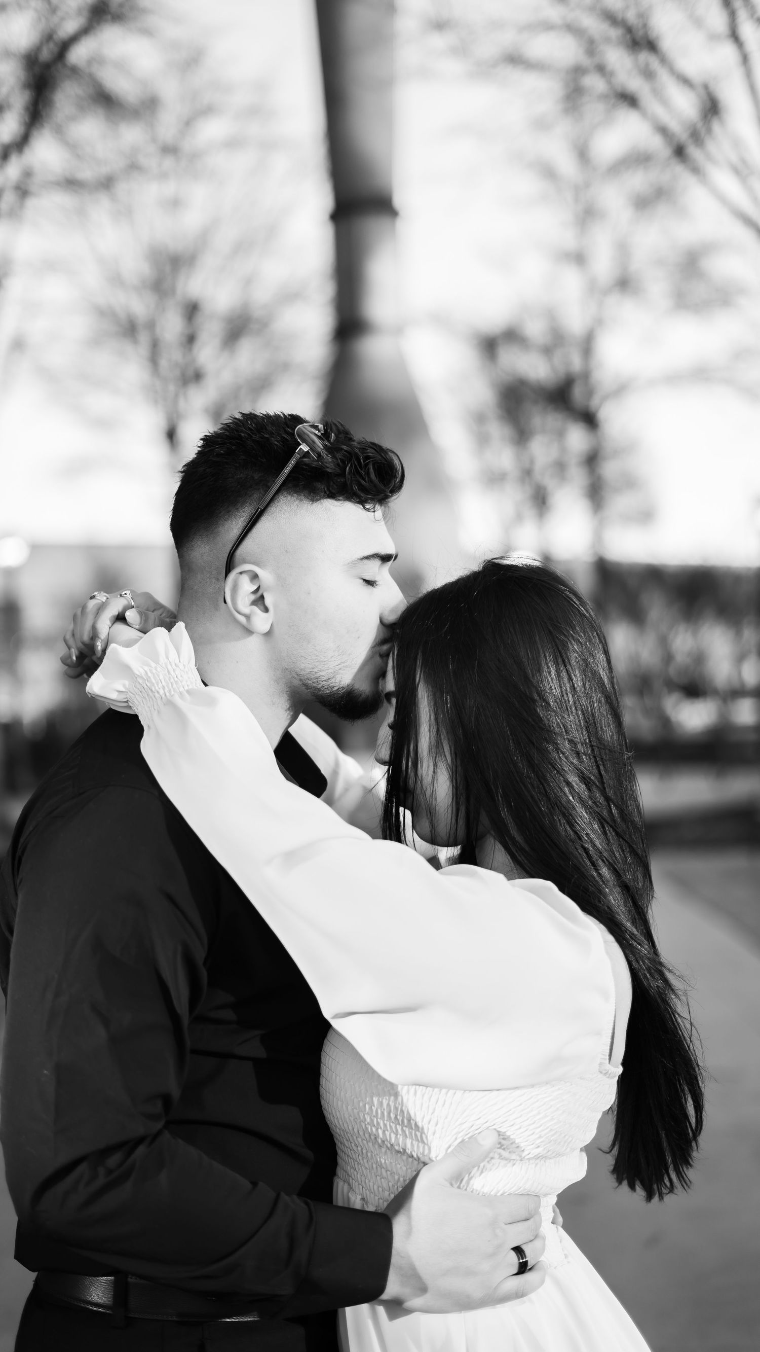 A couple shares an intimate moment in black and white photography under winter trees.