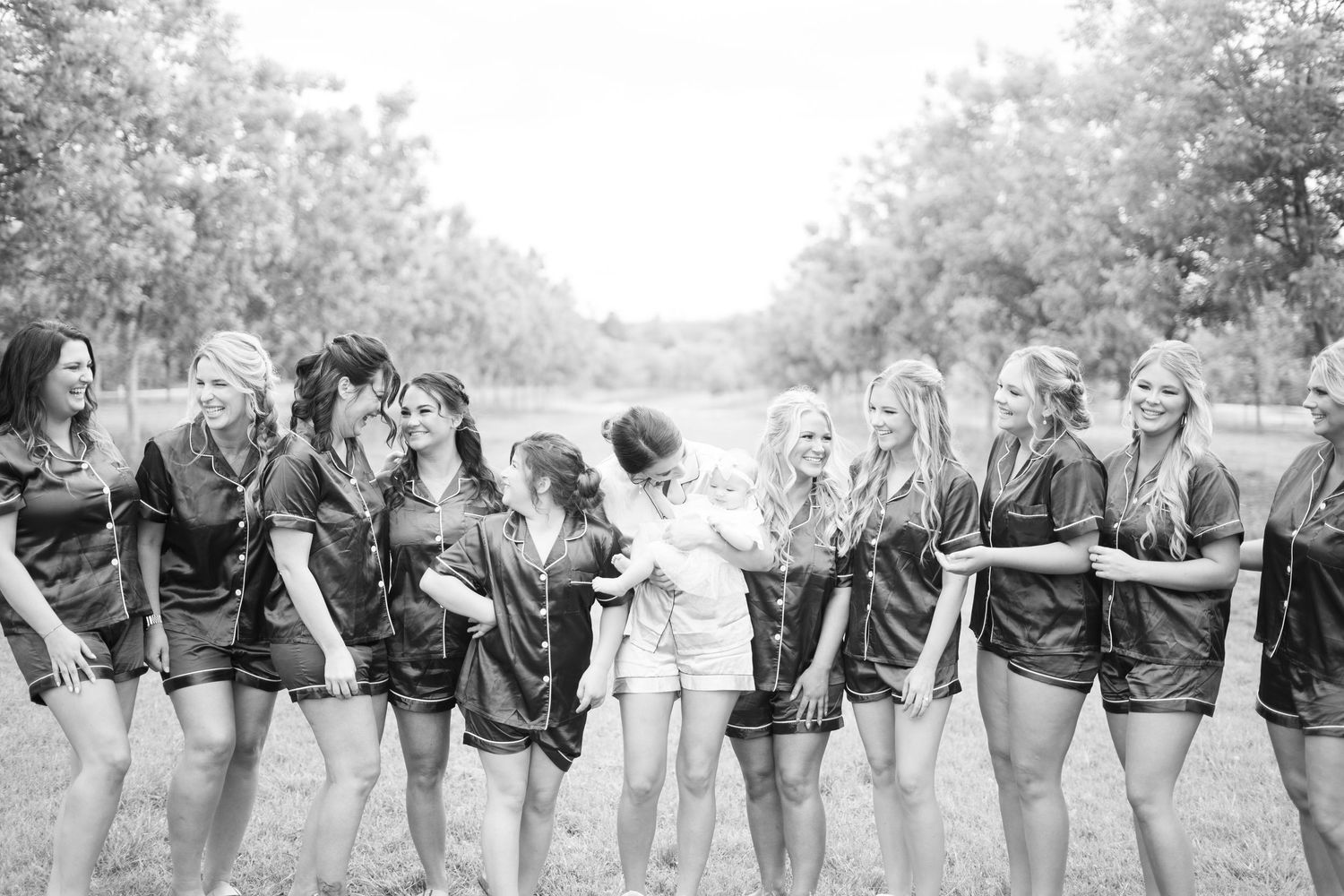 A row of people in black jackets lean forward while standing together outdoors in a creative group photo pose.