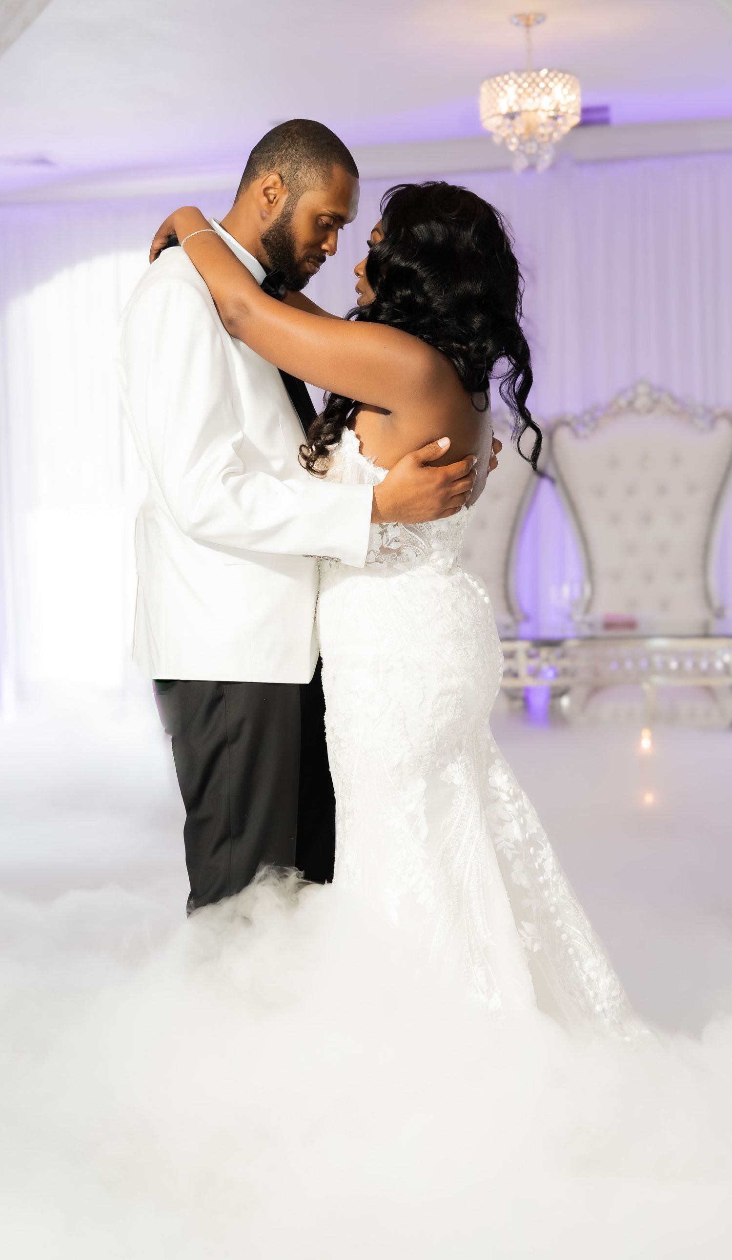 A romantic first dance at a wedding reception with misty fog and elegant purple lighting in an opulent ballroom setting.