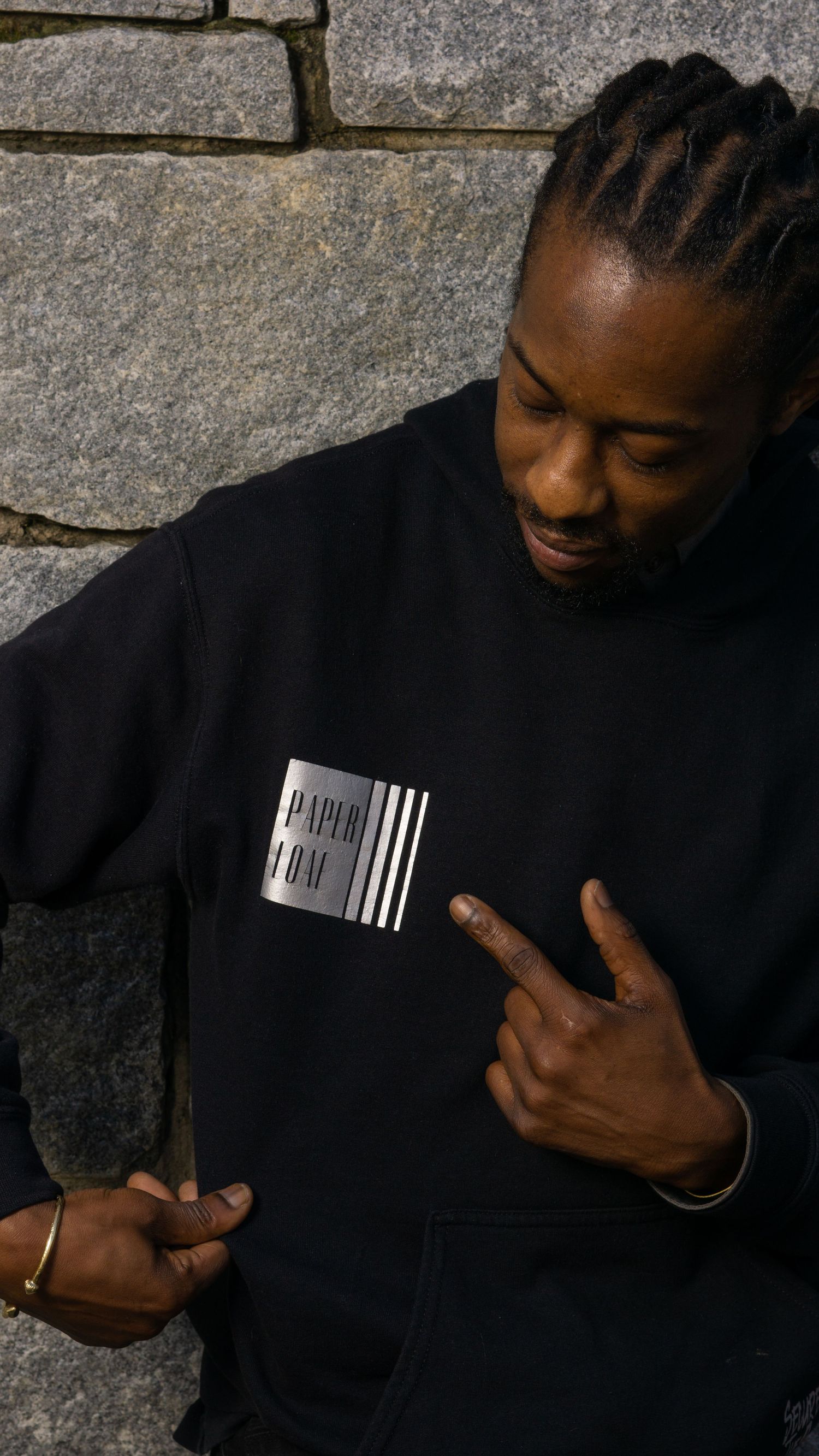 A person wearing a black sweatshirt with a barcode graphic design standing against a stone brick wall.