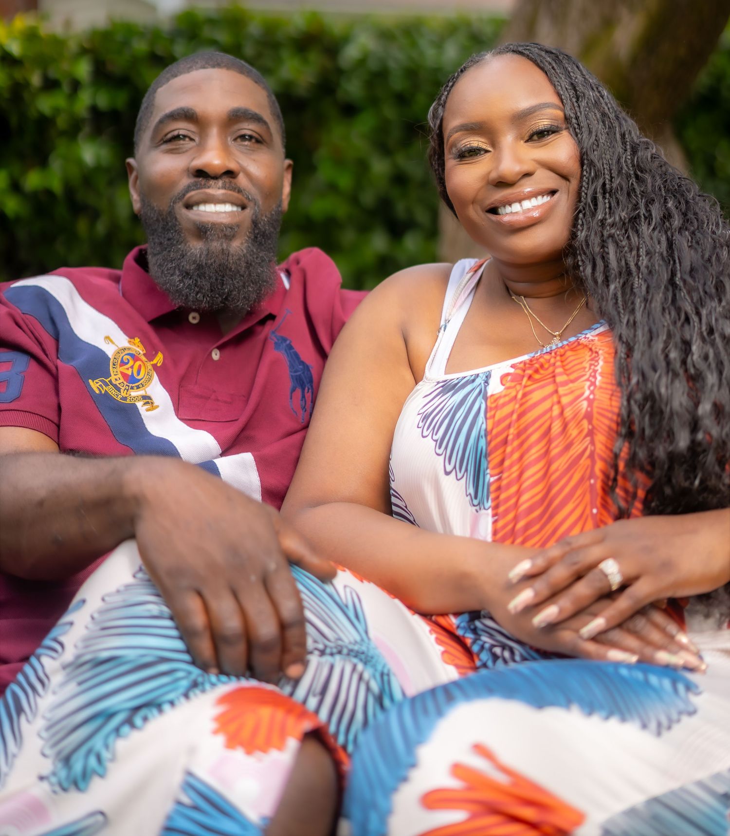 A smiling couple in colorful outfits sit closely together outdoors in a warm, relaxed portrait photo.