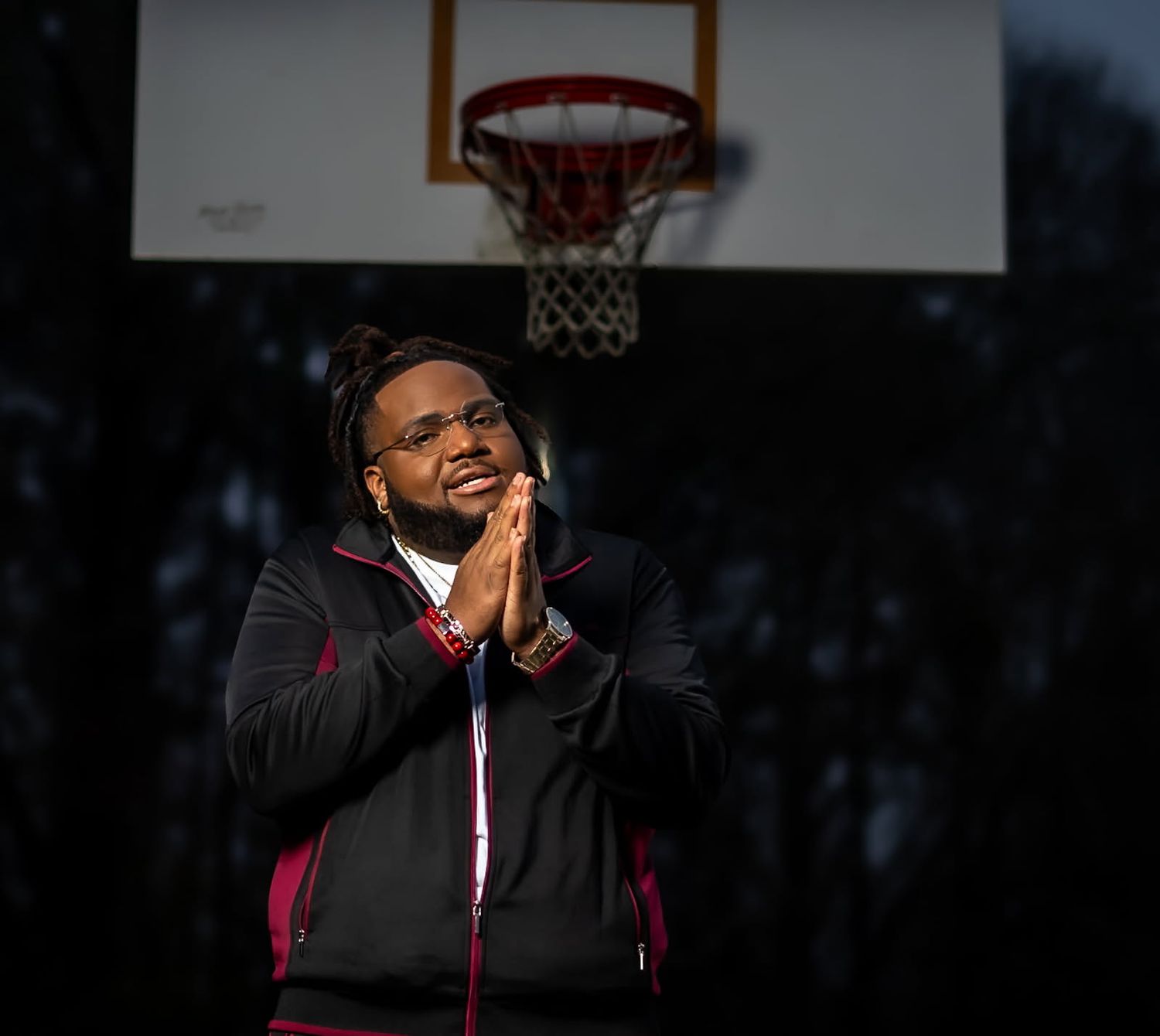 Person in dark jacket poses for a portrait in front of an outdoor basketball hoop at dusk.