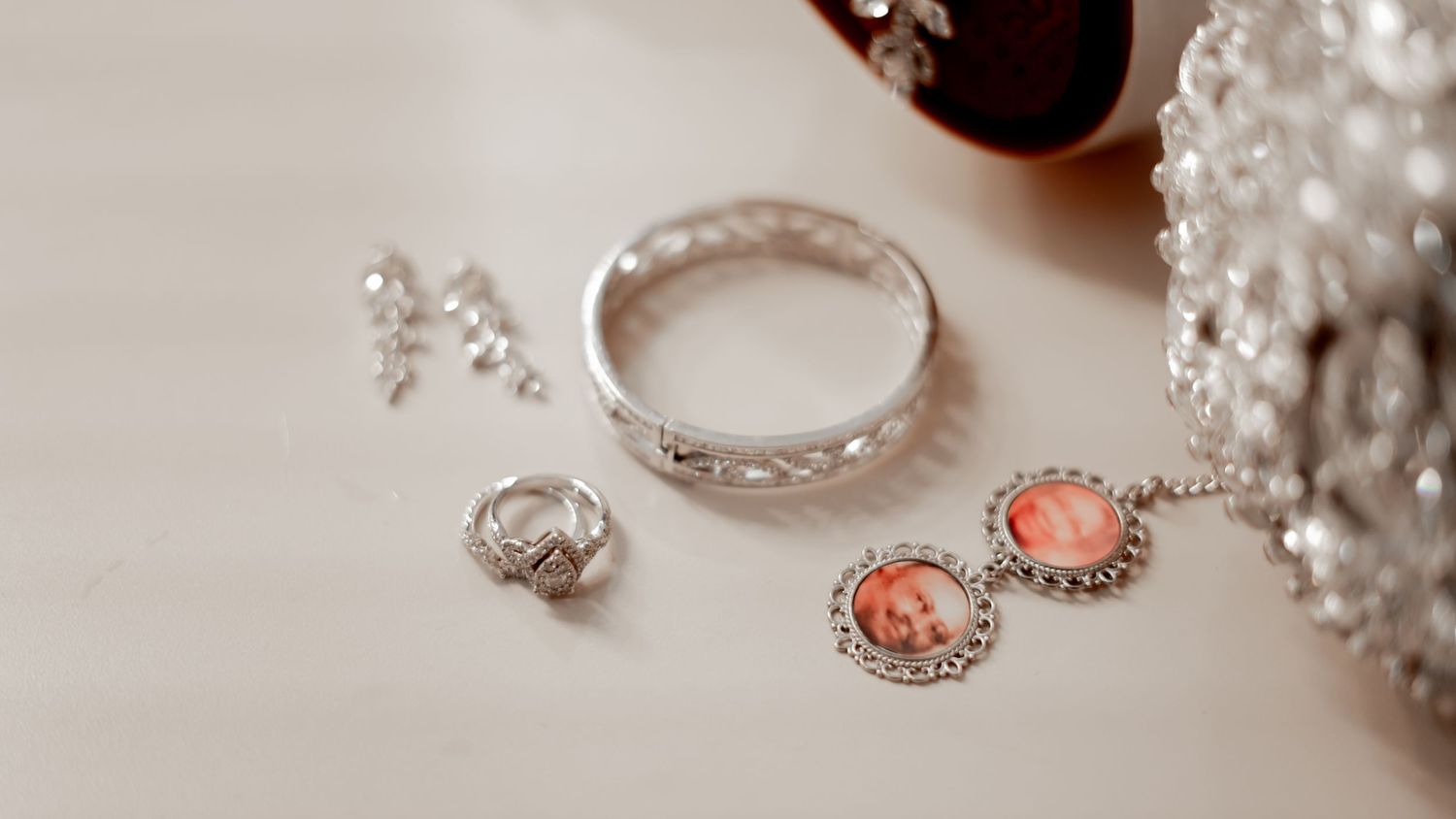 Delicate silver jewelry pieces including rings and coral-colored earrings arranged on a white surface.