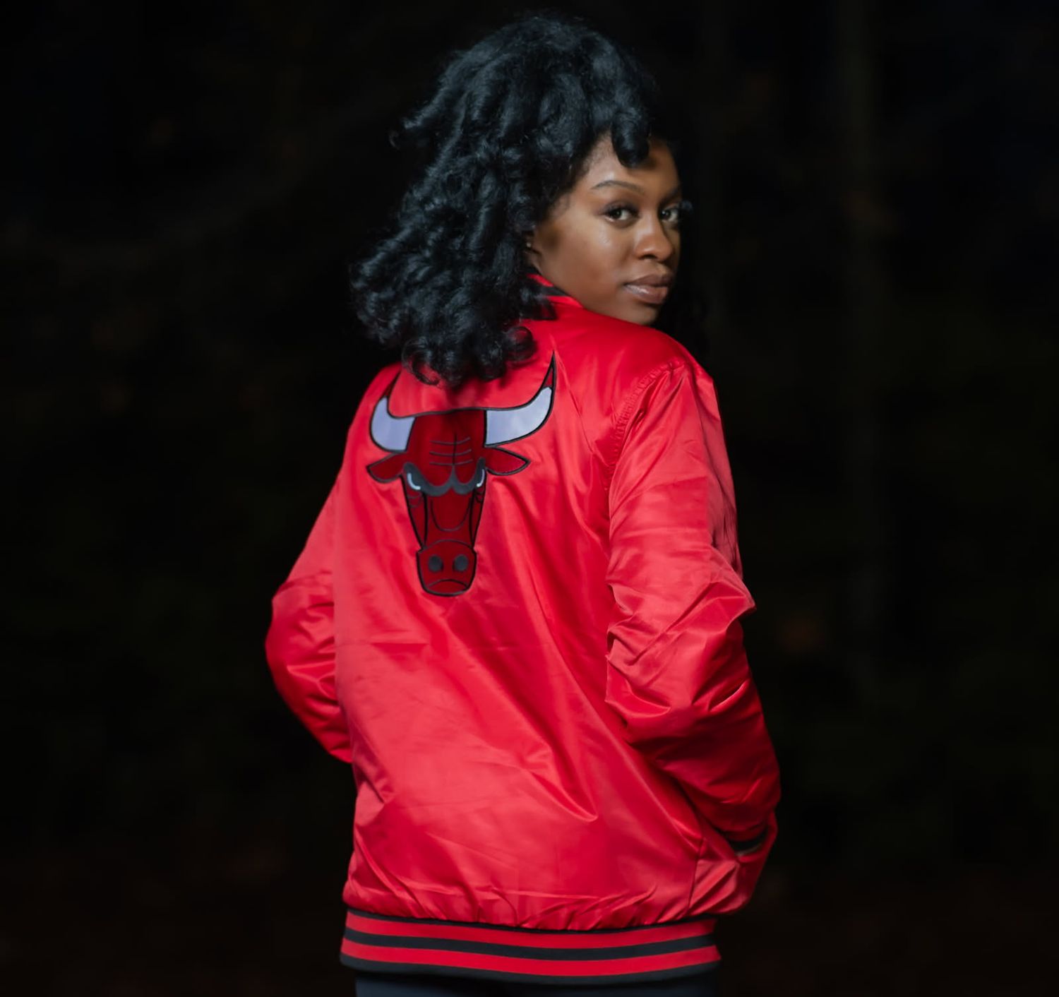A person wearing a bright red Chicago Bulls basketball jacket poses while looking over their shoulder.