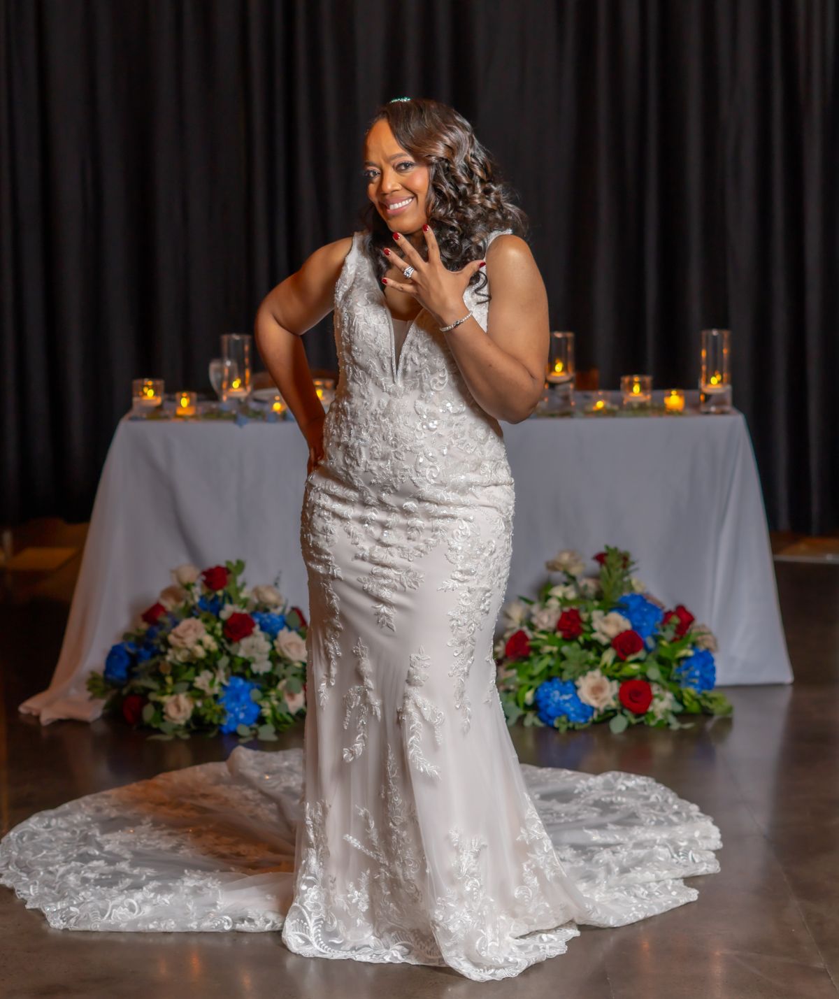 A radiant bride in a white lace gown poses for candid shots by a table with colorful floral arrangements.