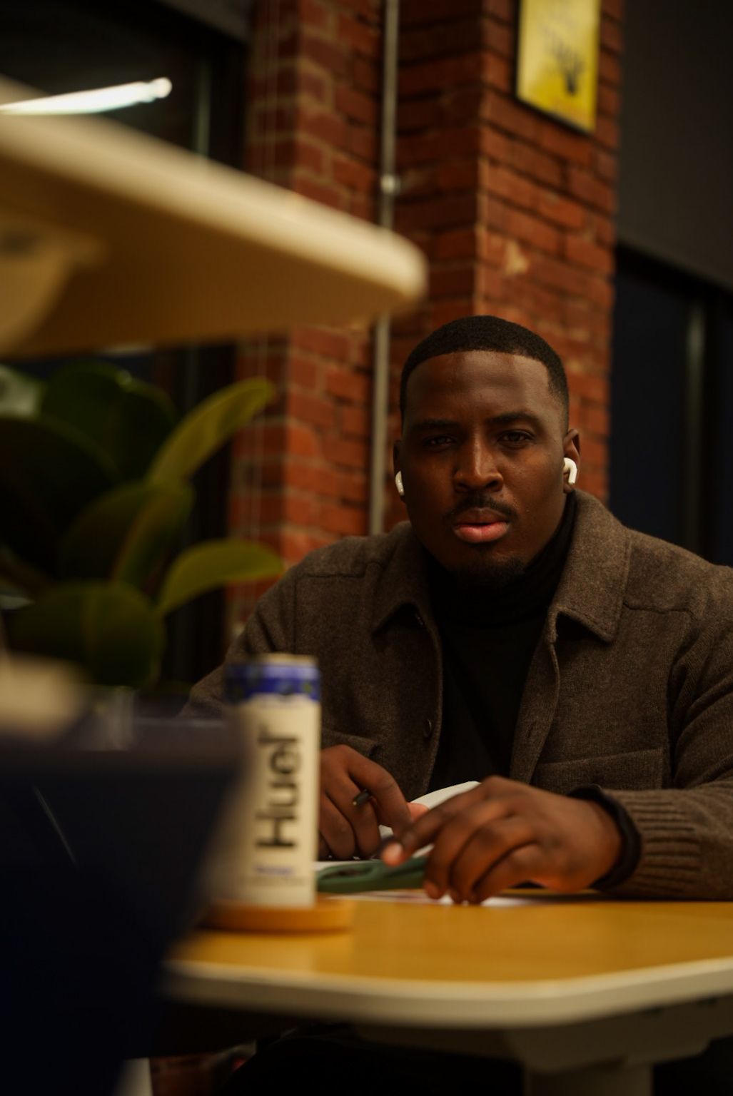 A person sits at a wooden table in a dimly lit room with brick walls and a coffee cup nearby.