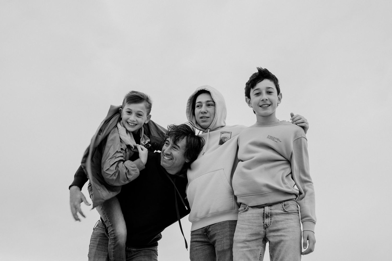 Group posing together against cloudy sky in casual black and white portrait.