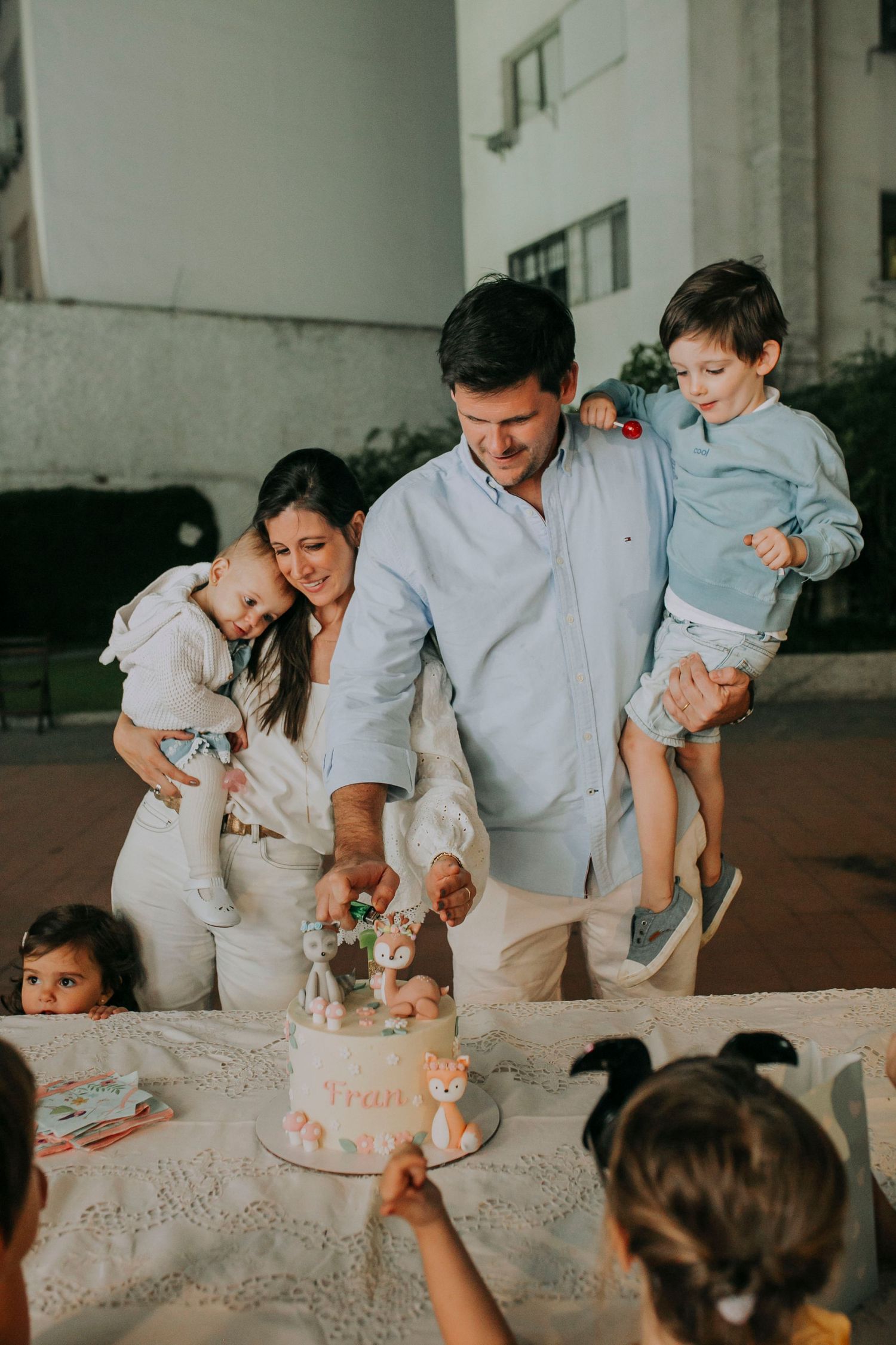 Family gathered around a birthday cake at an outdoor party celebration.