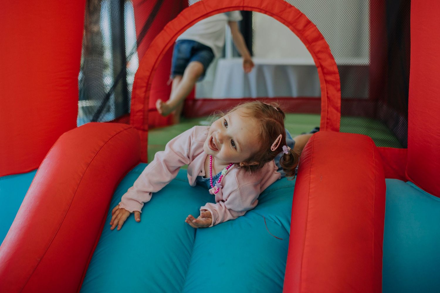 Small child playing and sliding on a colorful red and teal inflatable bounce house or playground equipment.
