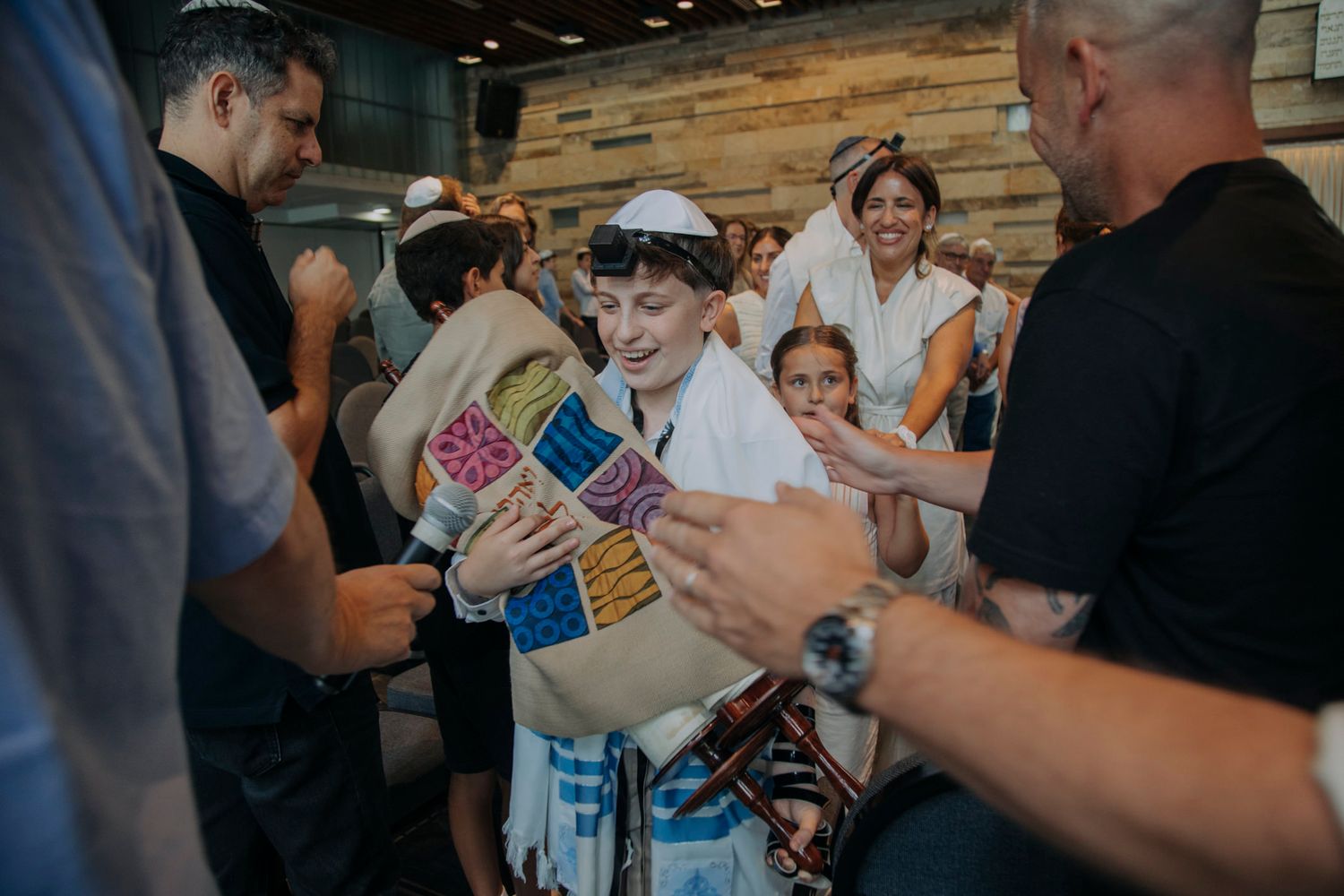 Young boy in tallit and kippah celebrated at his Bar Mitzvah ceremony surrounded by family and friends.