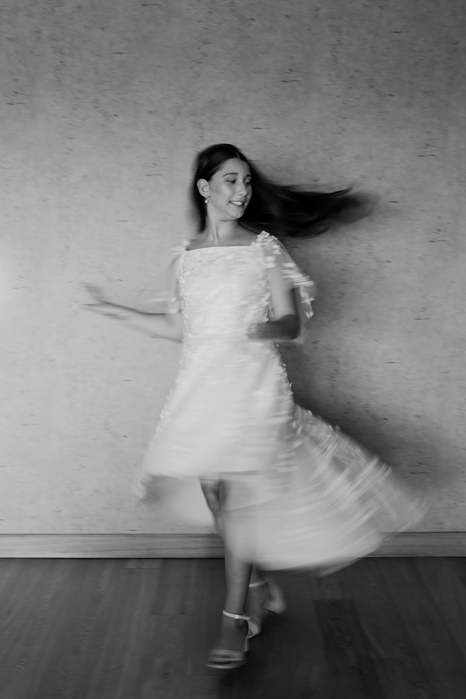 Black and white portrait of dancer twirling in a white dress with motion blur effect.