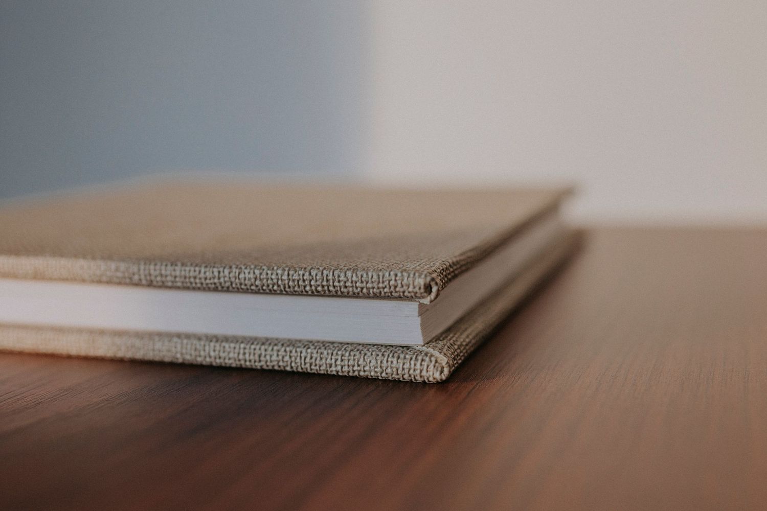 Minimalist photograph of linen-bound books stacked on wooden surface showing textural detail.