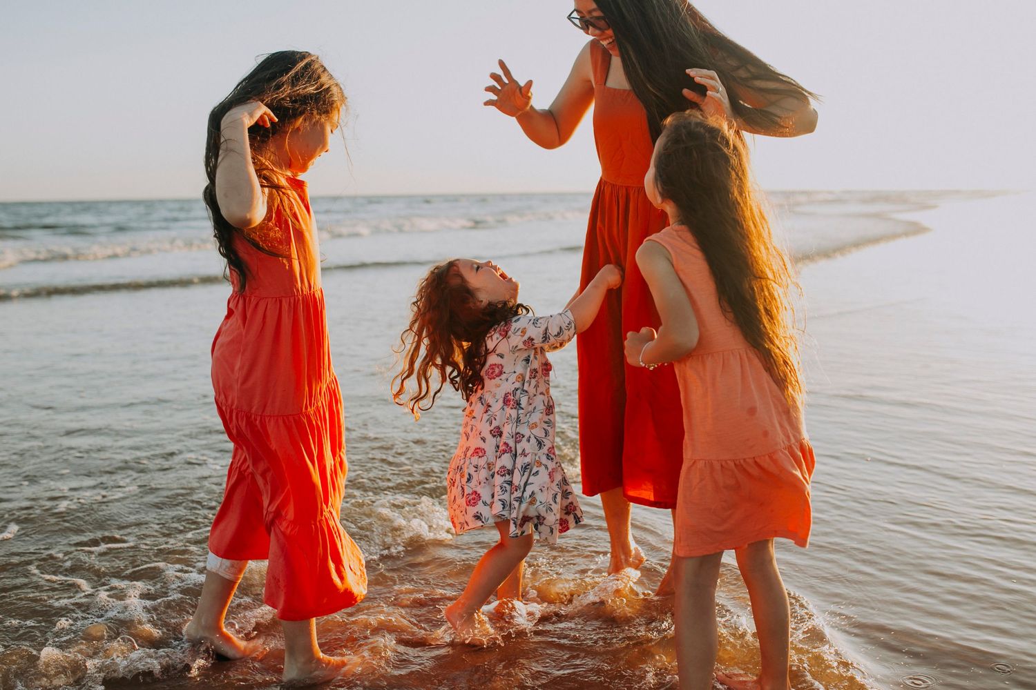 People in bright dresses playing and splashing in shallow ocean water.
