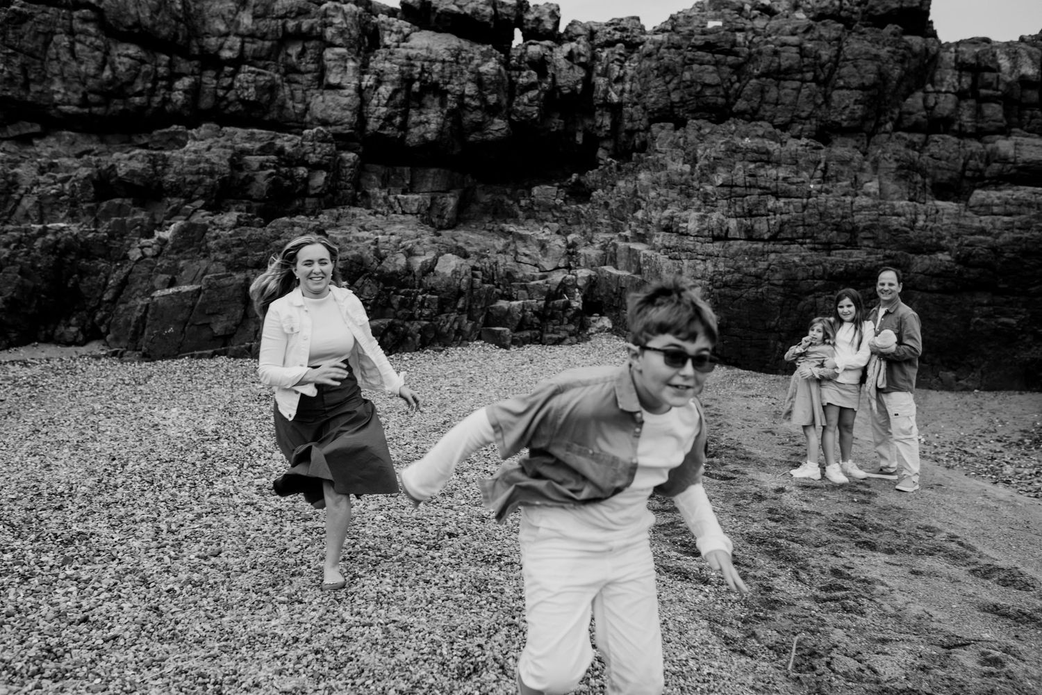 People enjoying a playful moment on a rocky beach with cliffs in the background.