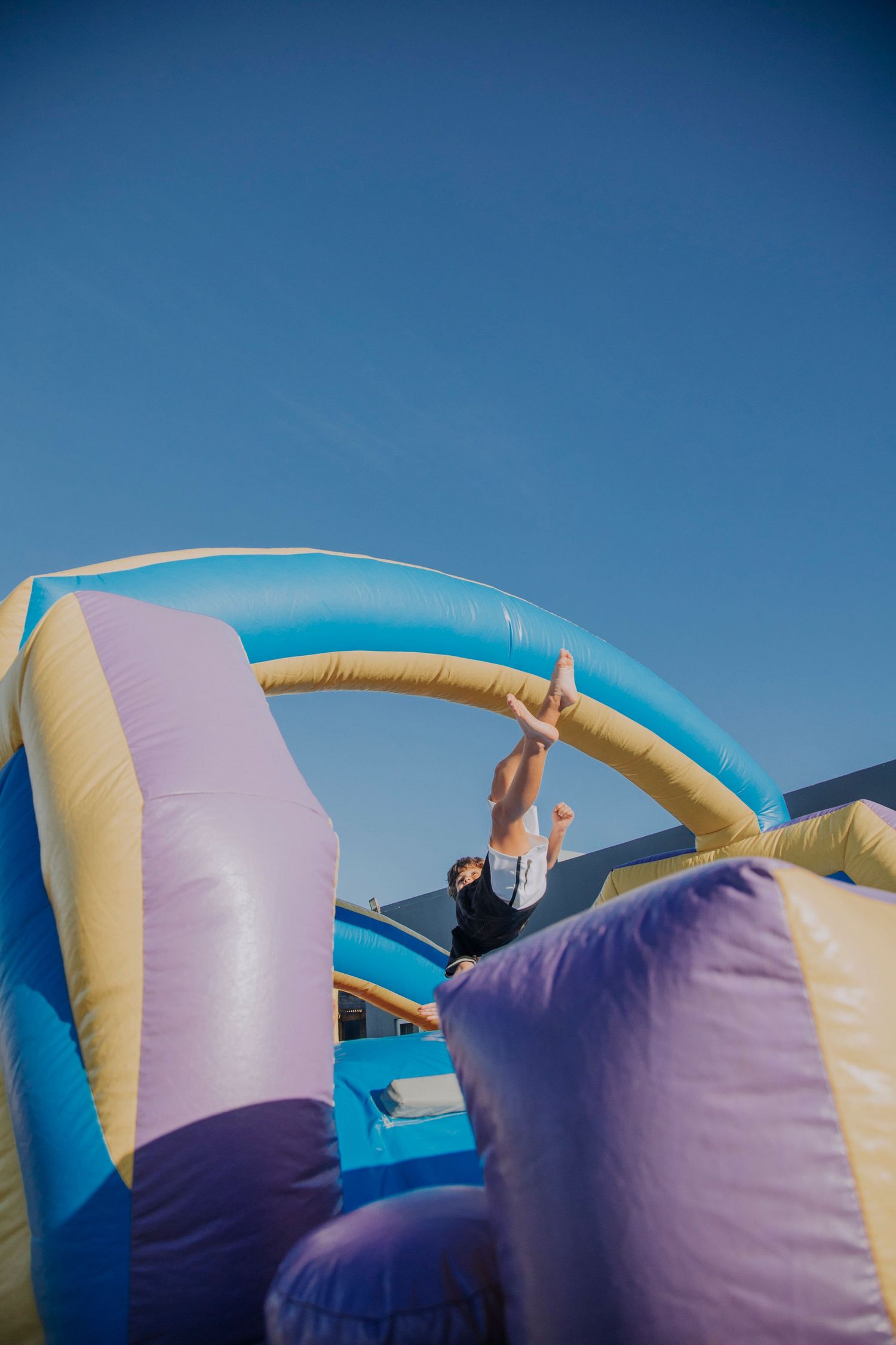 A person climbing up a colorful inflatable bounce house slide against a bright blue sky.