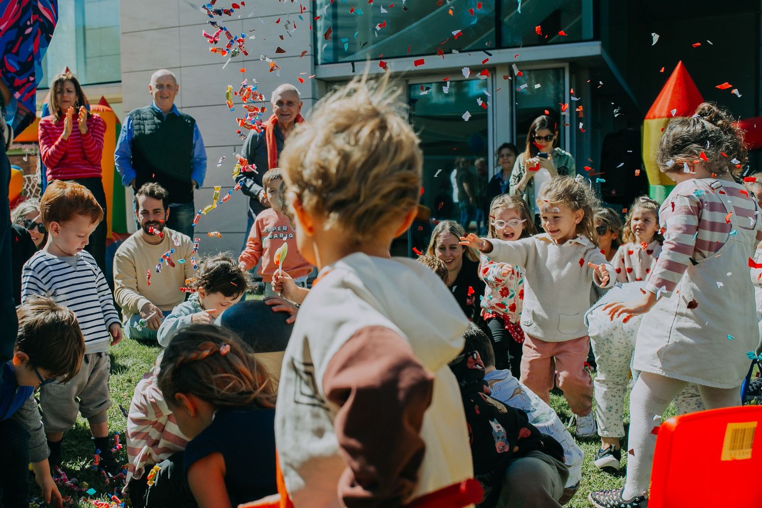 A festive outdoor celebration with children playing under falling confetti in a sunny garden party atmosphere.