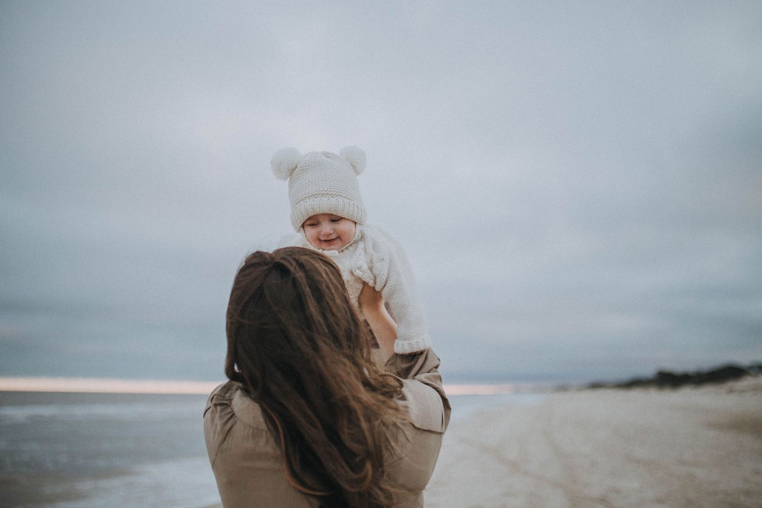 A tender moment captured on a misty beach, with a warm embrace against a moody winter sky.