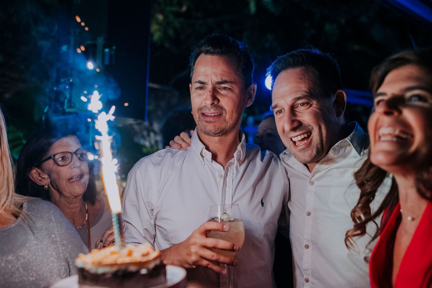 Party guests enjoying sparklers and drinks during an outdoor nighttime celebration.