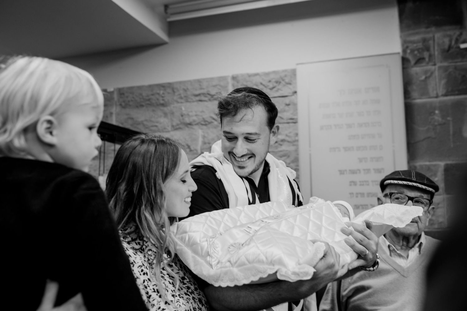 Intimate black and white moment of a family gathering around a swaddled infant.