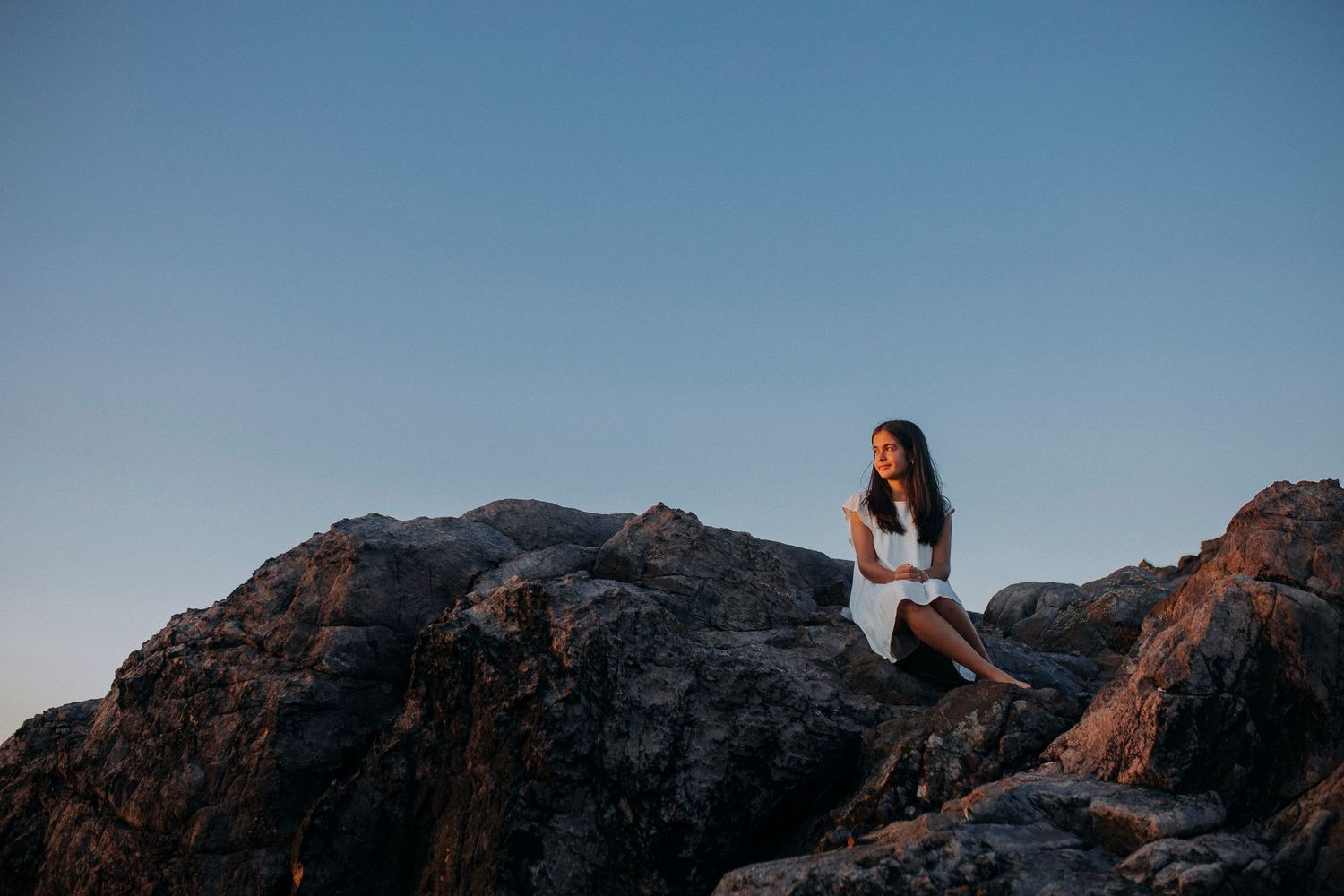 A person in white sits atop rocky mountain terrain against a blue sky.